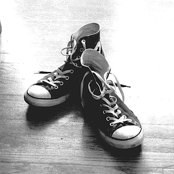 A pair of black high-top sneakers with white soles and laces on a wooden floor, with one shoe's tongue pulled out.