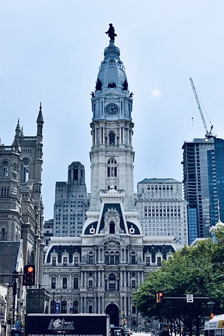 Philadelphia City Hall with historic architecture and a clock tower, surrounded by modern skyscrapers and city streets.