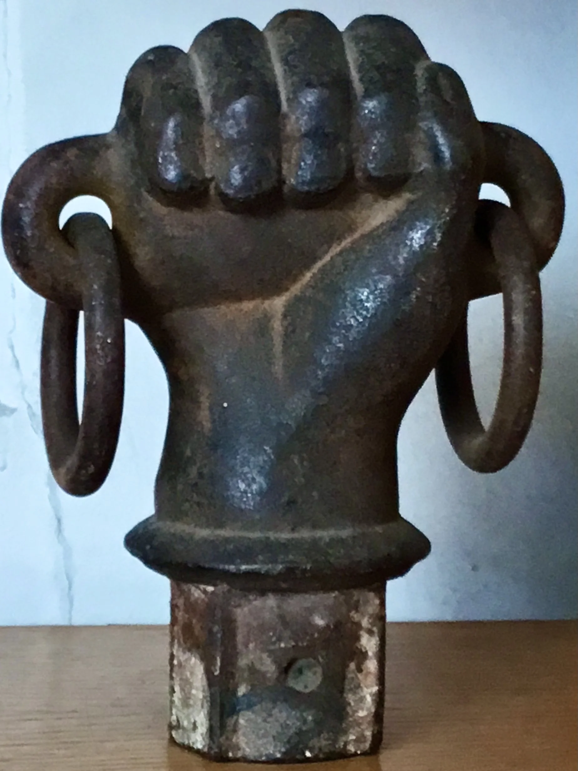 A vintage metal sculpture of a clenched fist with large circular earrings, mounted on a rectangular base.