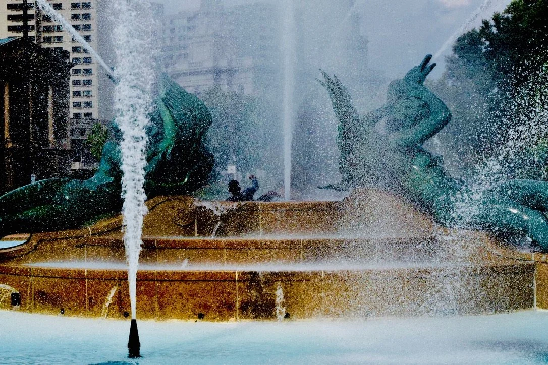 Close-up of a fountain with two dolphin sculptures spraying water in an urban setting.