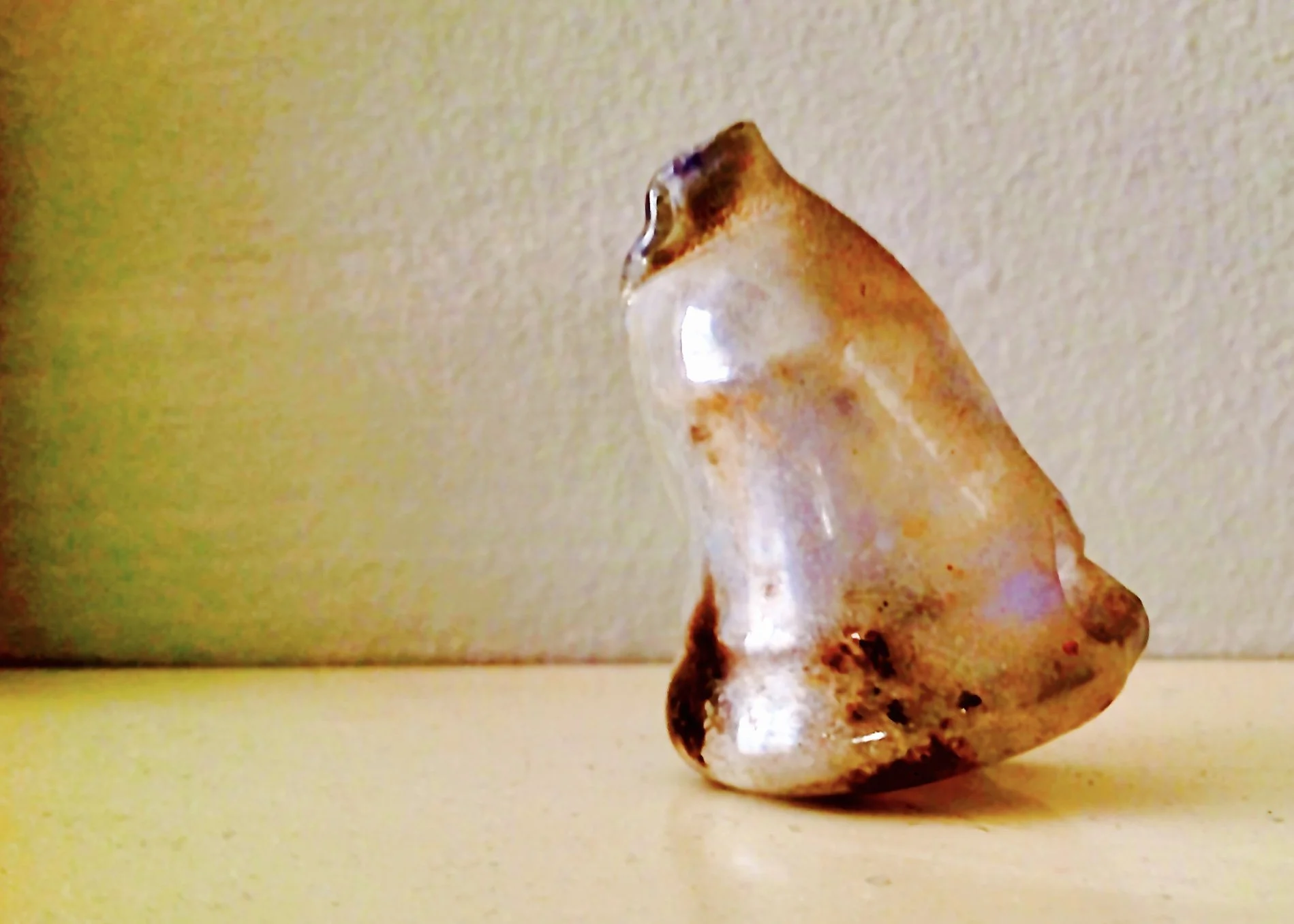 A polished, irregularly shaped brown, white, and clear gemstone sitting on a flat surface against a plain background.