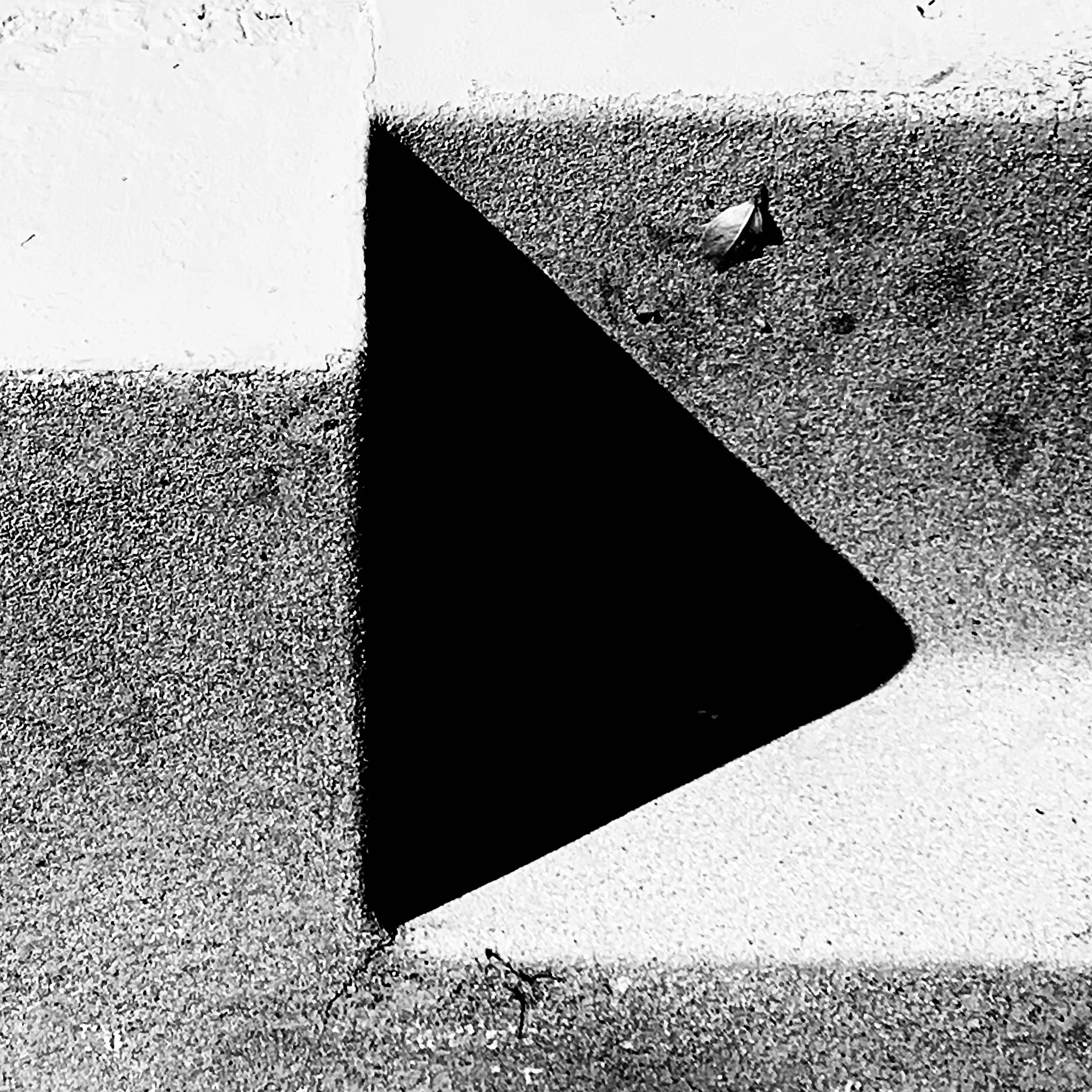 Close-up of a black painted triangle on a textured, speckled surface with a small screw and some leaves nearby.