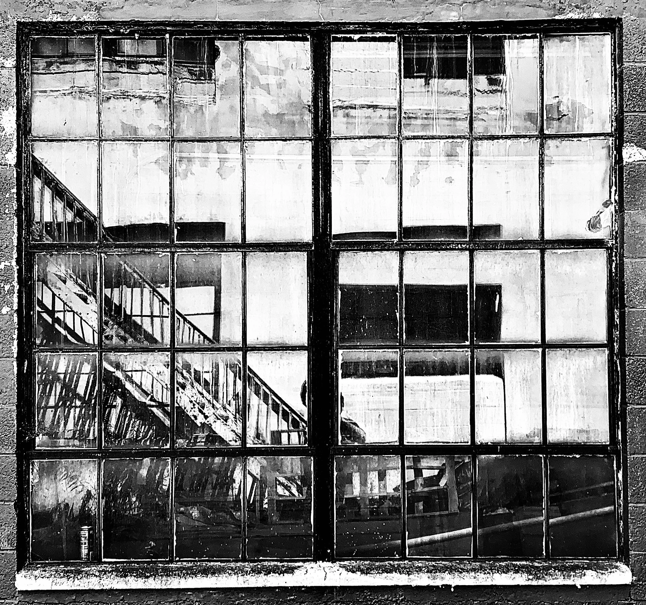 Black and white photo of a large window with multiple panes, reflecting a staircase inside a building.