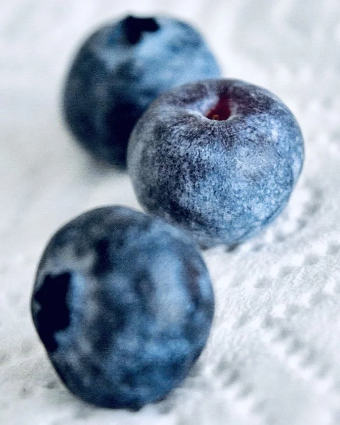 Close-up of three blueberries on a textured white surface.
