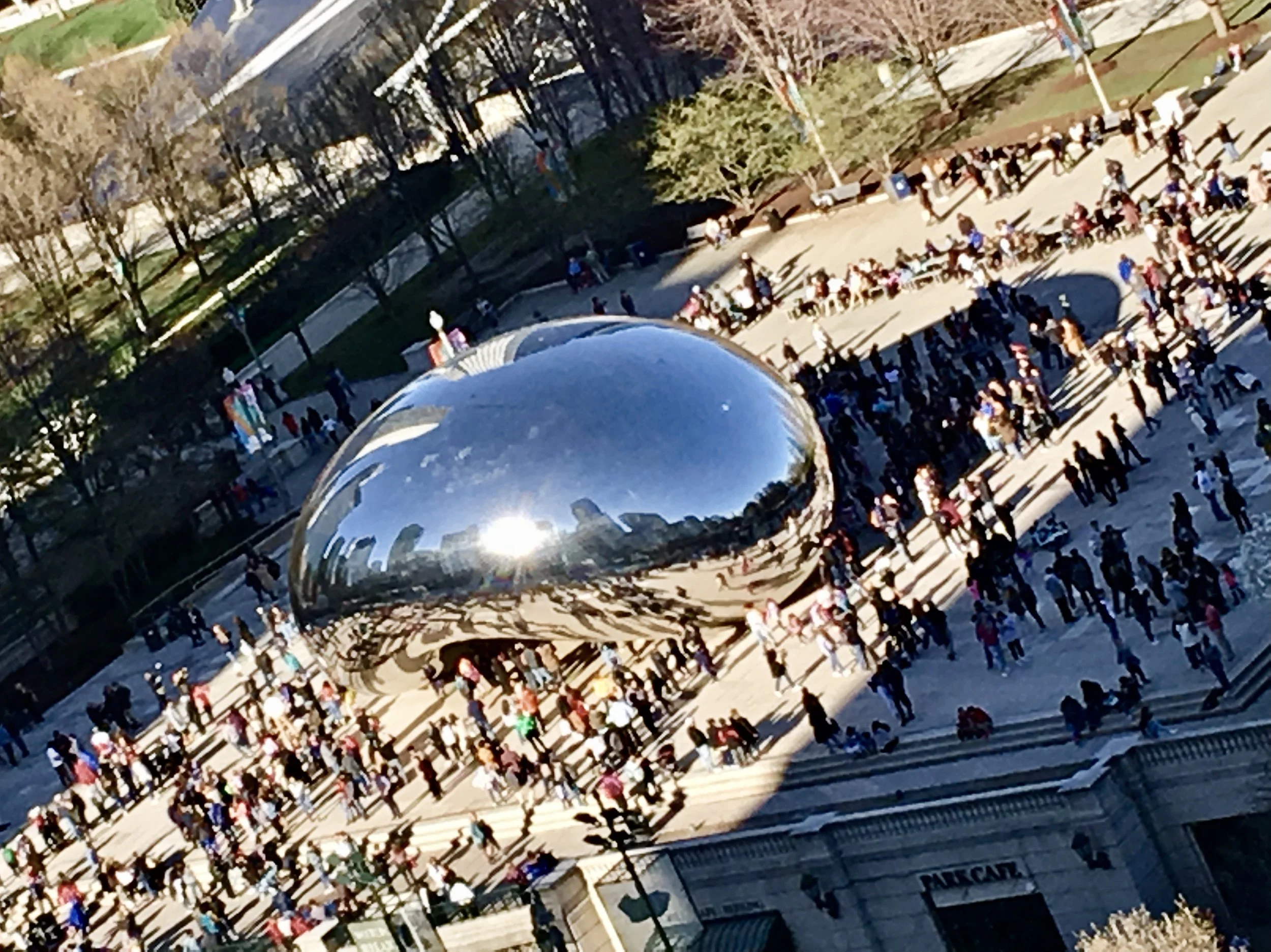 Chicago Millennium Park's Cloud Gate sculpture, also called 'The Bean,' with people walking around and crowds gathering in the plaza on a sunny day.