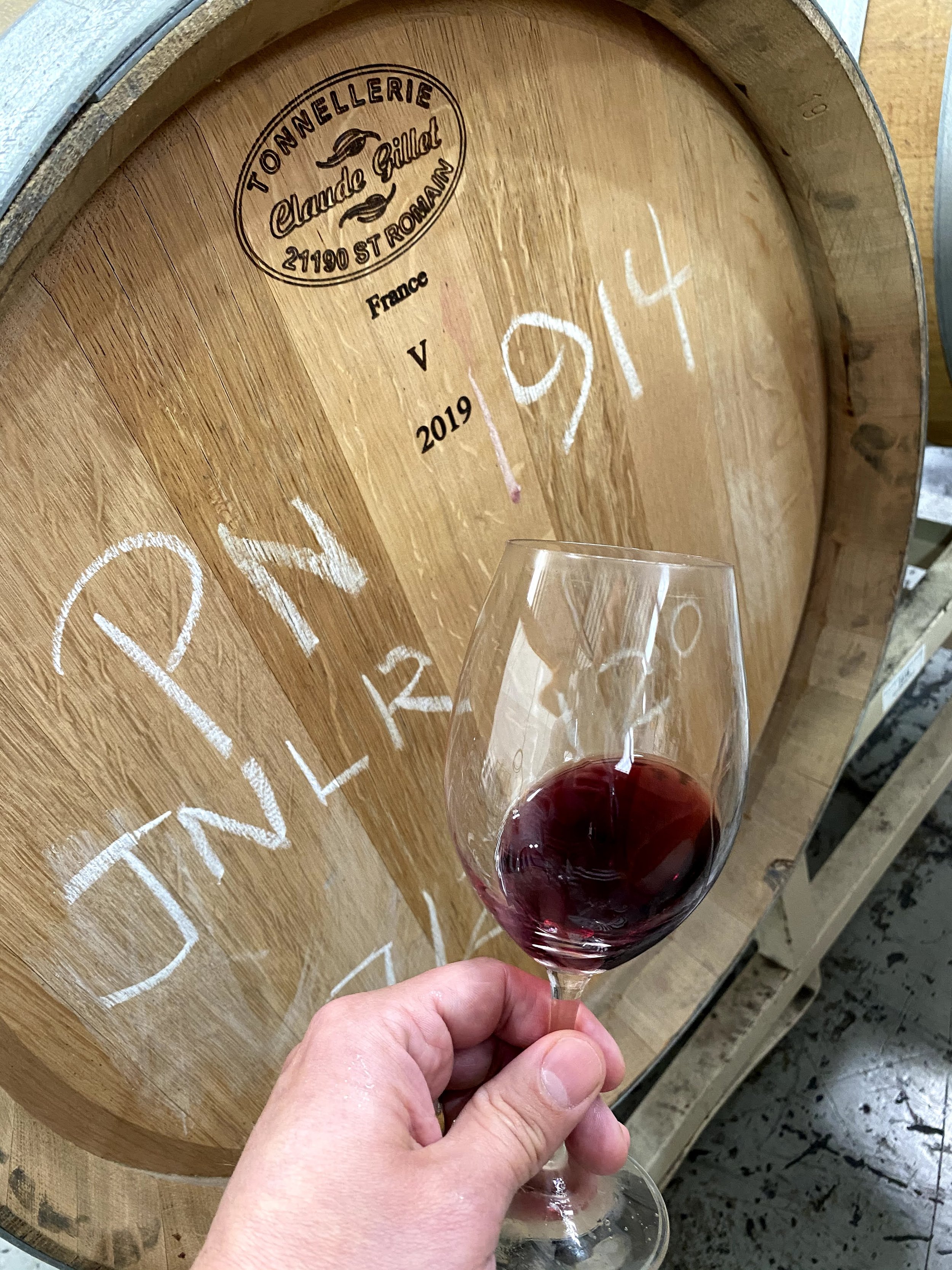 Hand swirling a glass of Joyful Noise red wine in front of a barrel