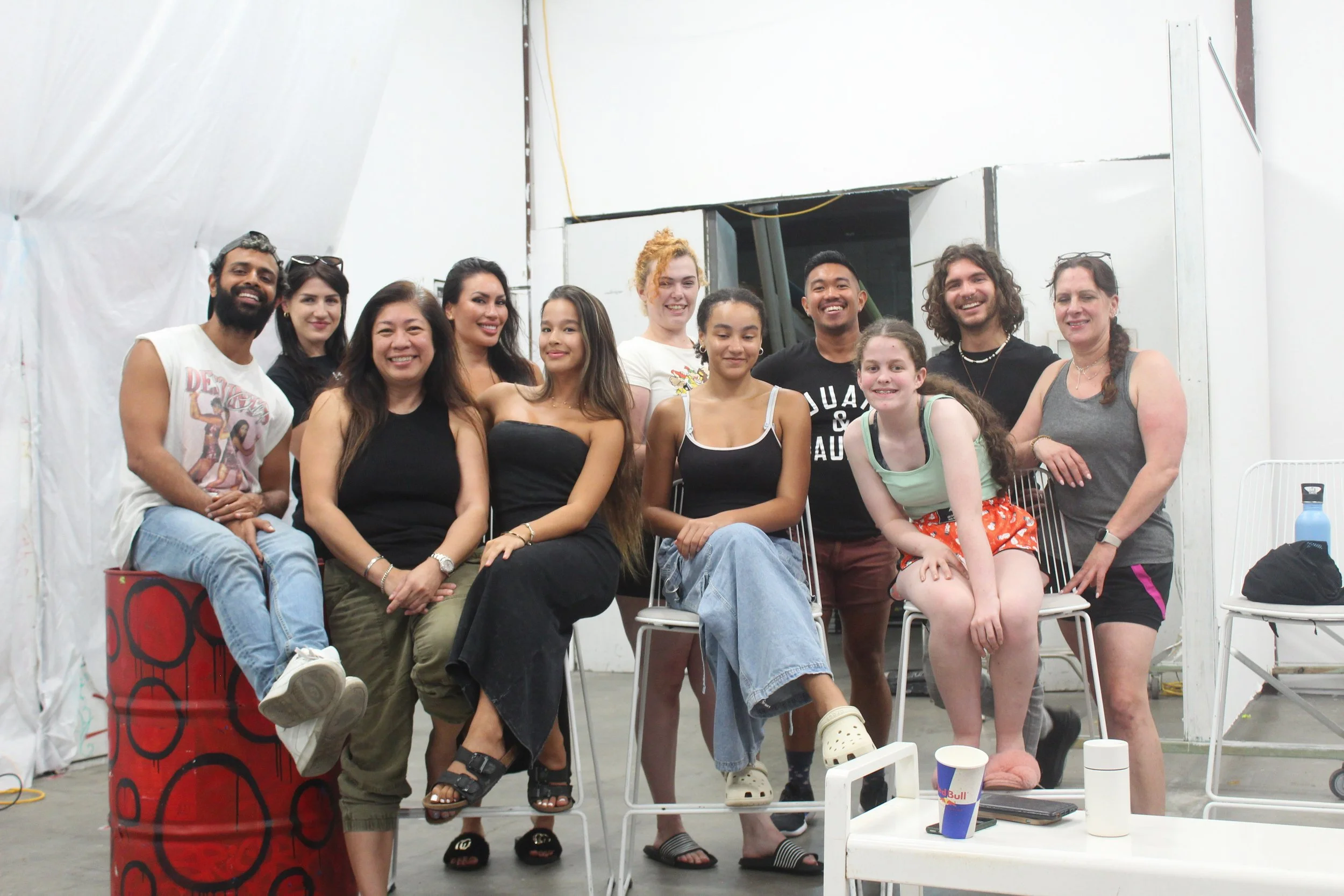 A diverse group of people smiling and posing together in an indoor setting with white walls and casual clothing.