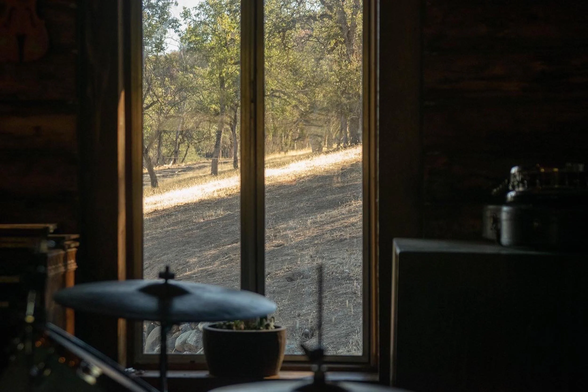 View through a window showing a dirt path with grass and trees in a rural area during daytime.