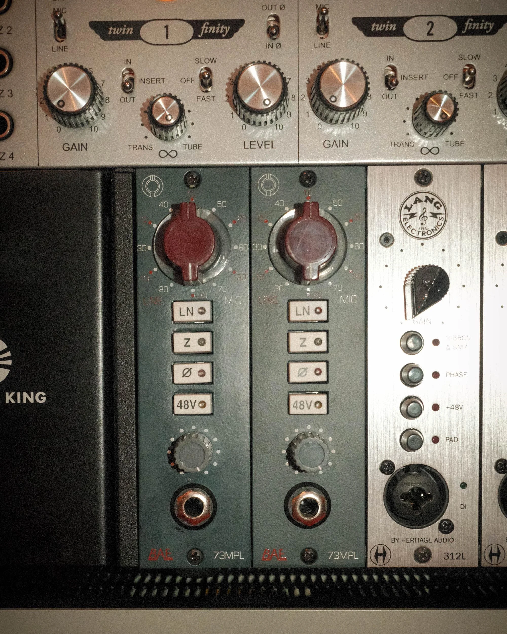 Close-up of audio equipment featuring a professional mixing console with multiple knobs, switches, and input/output connectors, including two large red knobs labeled '48V' for phantom power, and various sliders and buttons for adjusting sound levels 