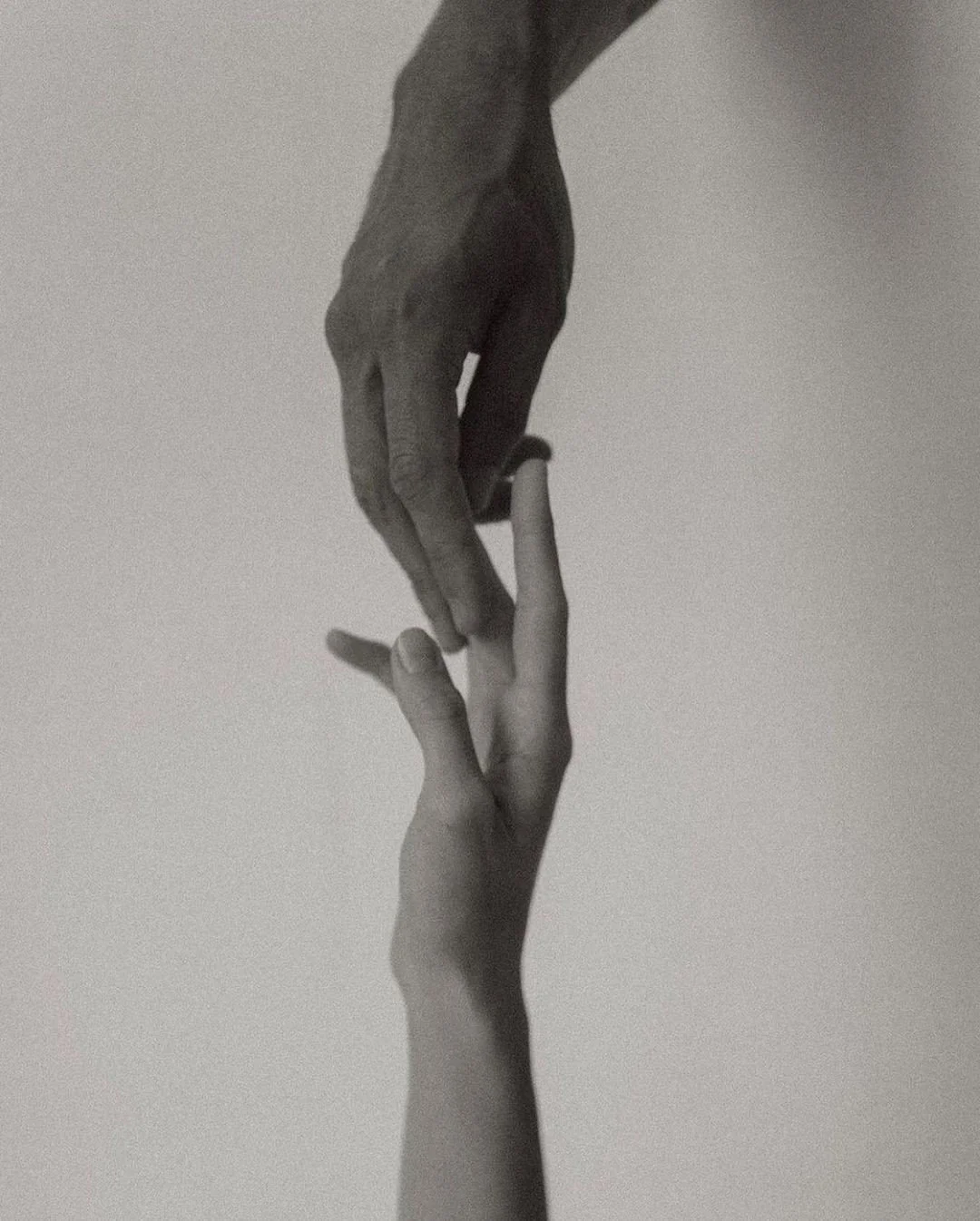 Dos manos, una adulta y una infantil, tocándose suavemente con los dedos casi entrelazados.