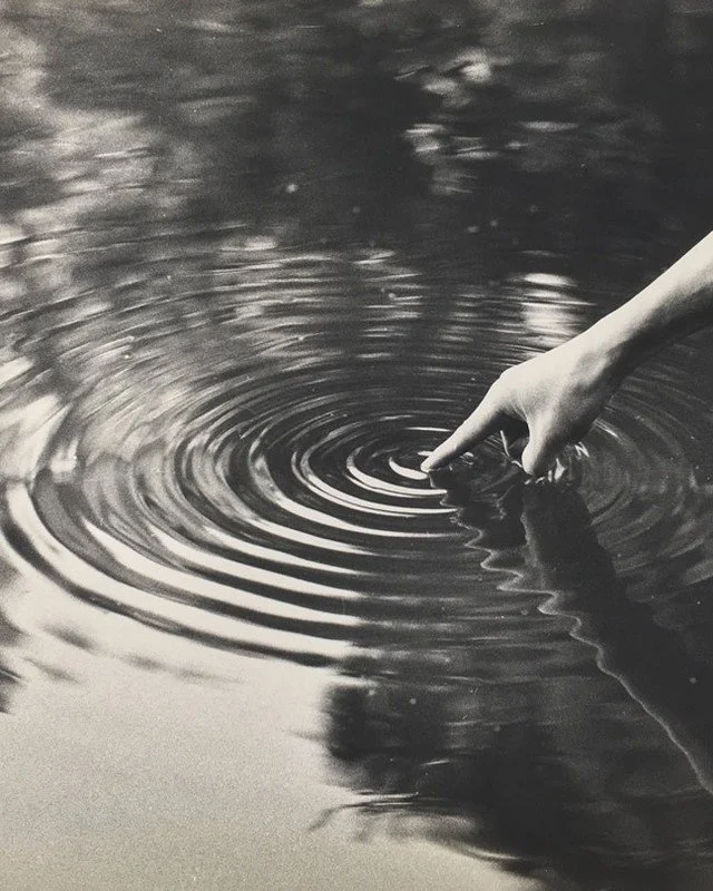 Una mano tocando la superficie del agua creando ondas concéntricas.