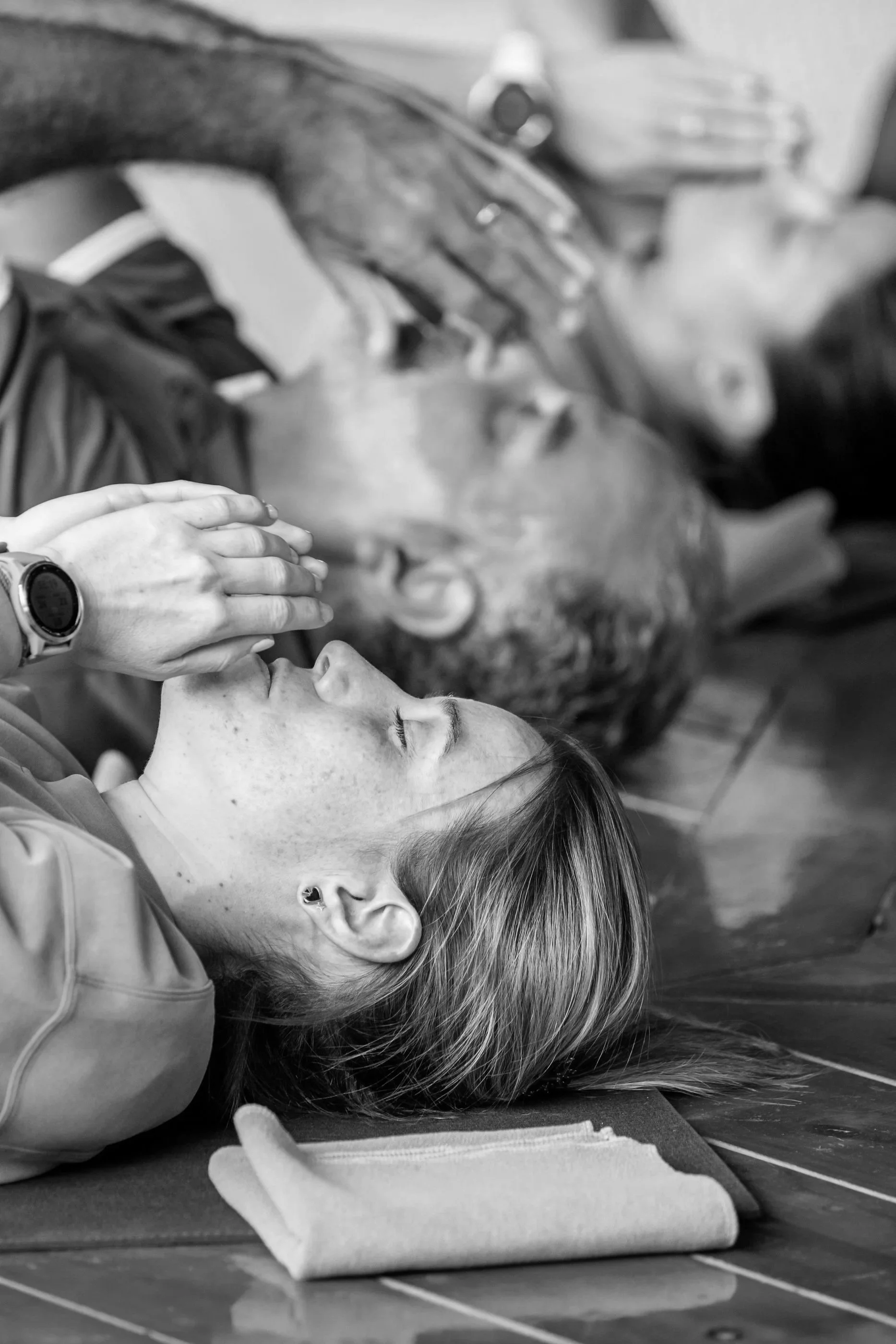 Persona acostada en el suelo con los ojos cerrados, recibiendo una bendición o oración de una mano que está sobre su rostro.