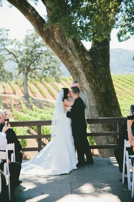 BR Cohn Winery wedding bride and groom's first kiss under old oak tree and vineyards behind
