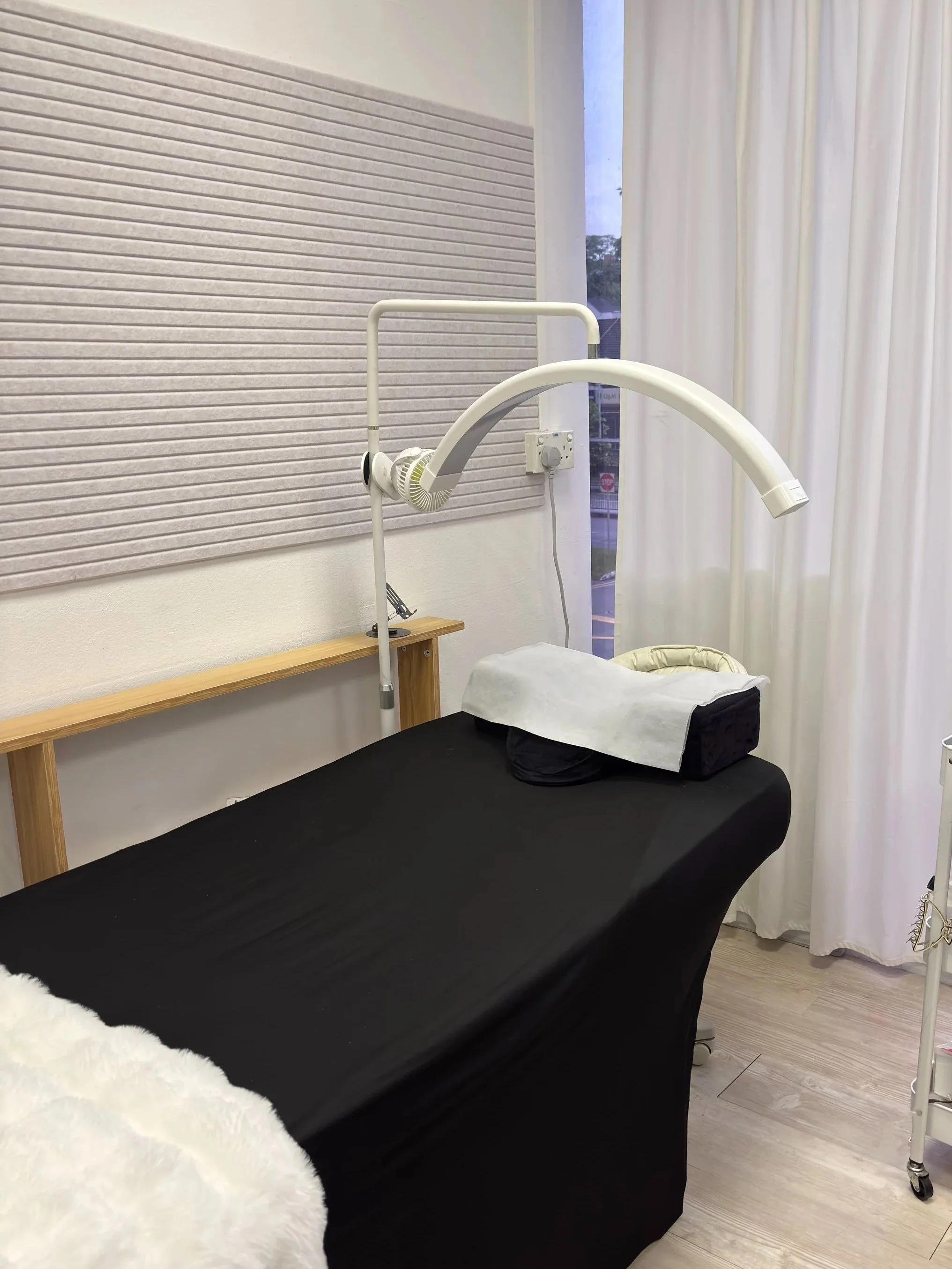 Hospital examination room with black bed, medical light, and white curtains.