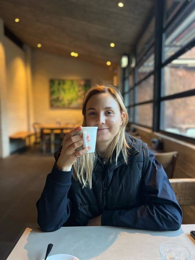 Person holding a coffee cup sitting in a cafe with large windows and modern decor.