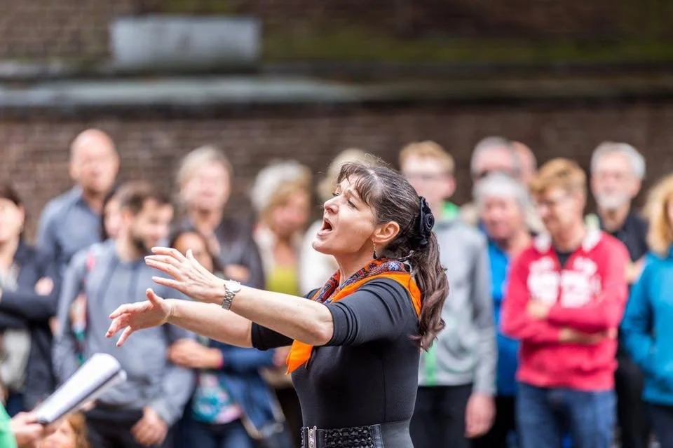 Dirigent Tatiana Lina leidt enthousiast een koor tijdens een optreden in de buitenlucht