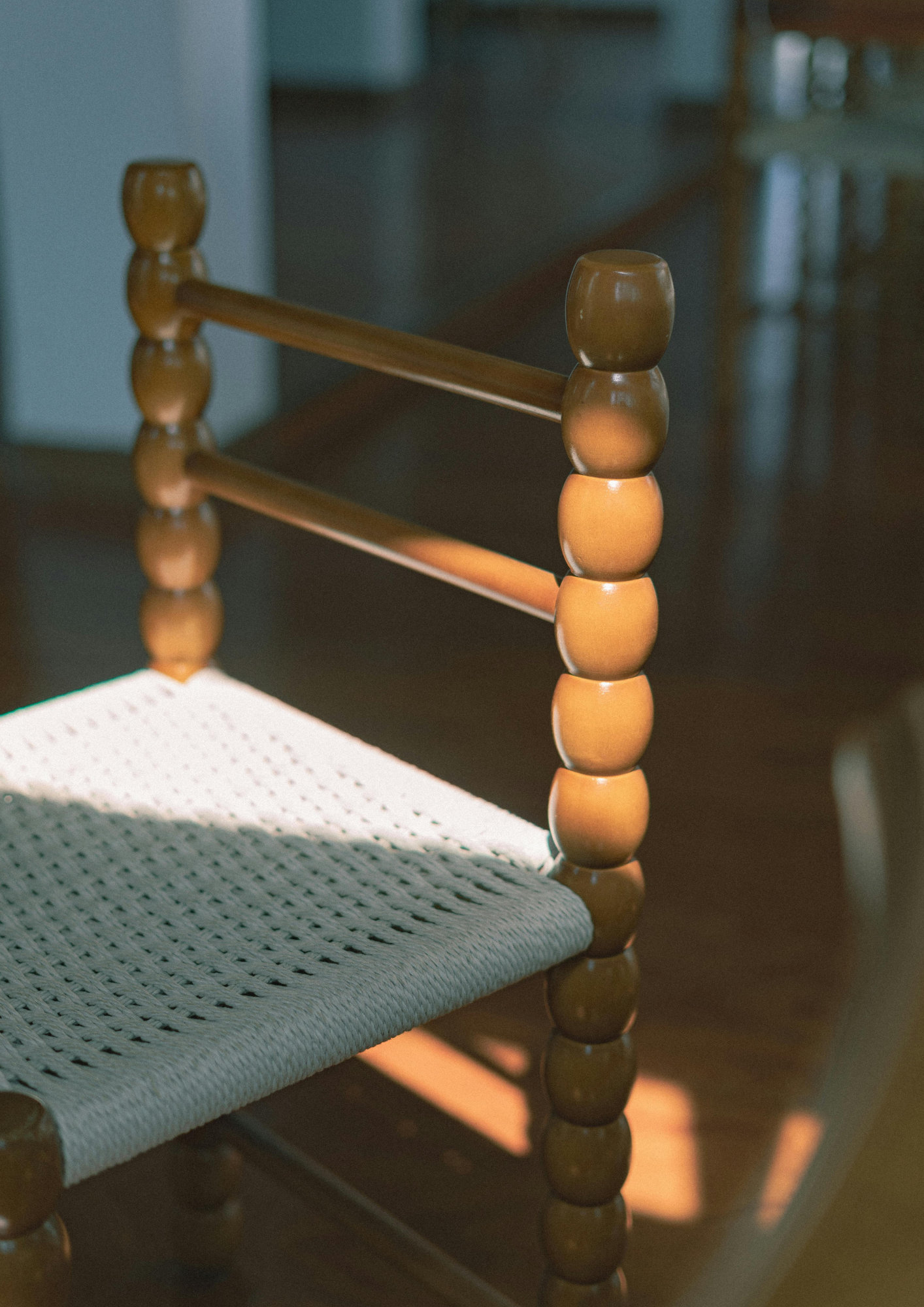 A wooden spindle chair with a woven seat in window light, with shadows falling across the floor. Design Mood by ARDISENOSTUDIO