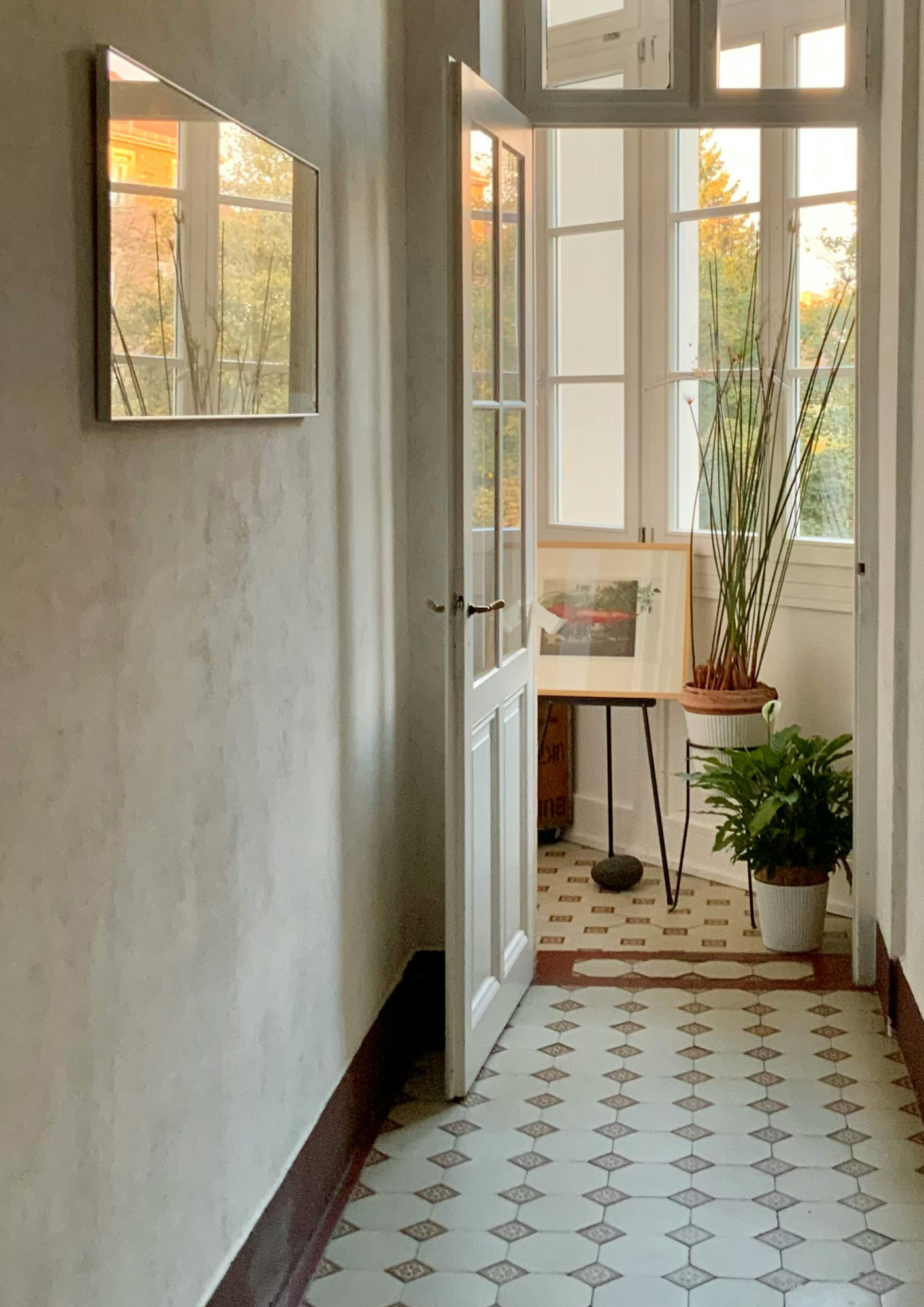 A view through an open doorway down a hallway to a tall window, with light falling on the parquet floor. Design Mood by ARDISENOSTUDIO
