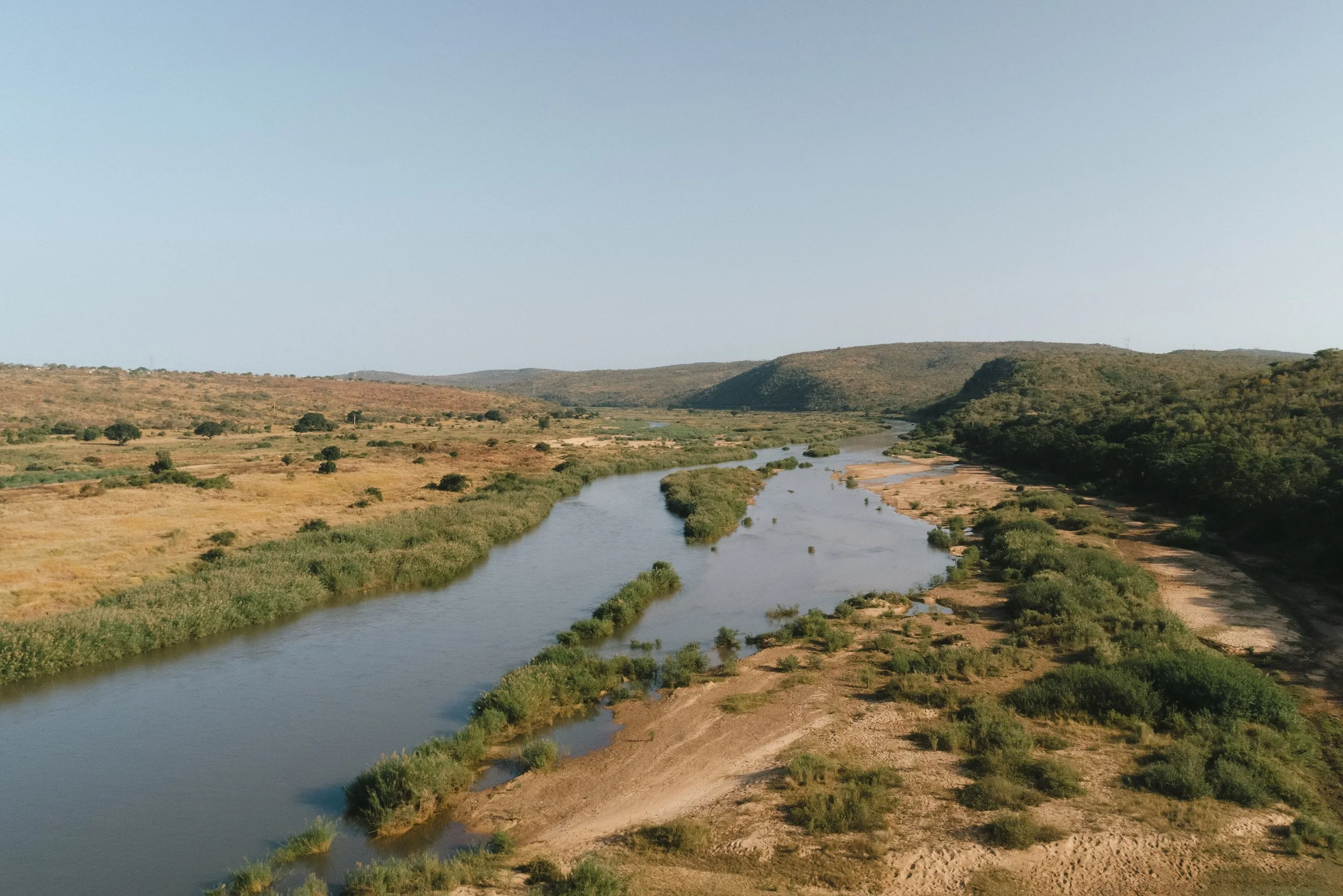 A wide view of a river flowing through an arid landscape with sparse vegetation and hills in the background.