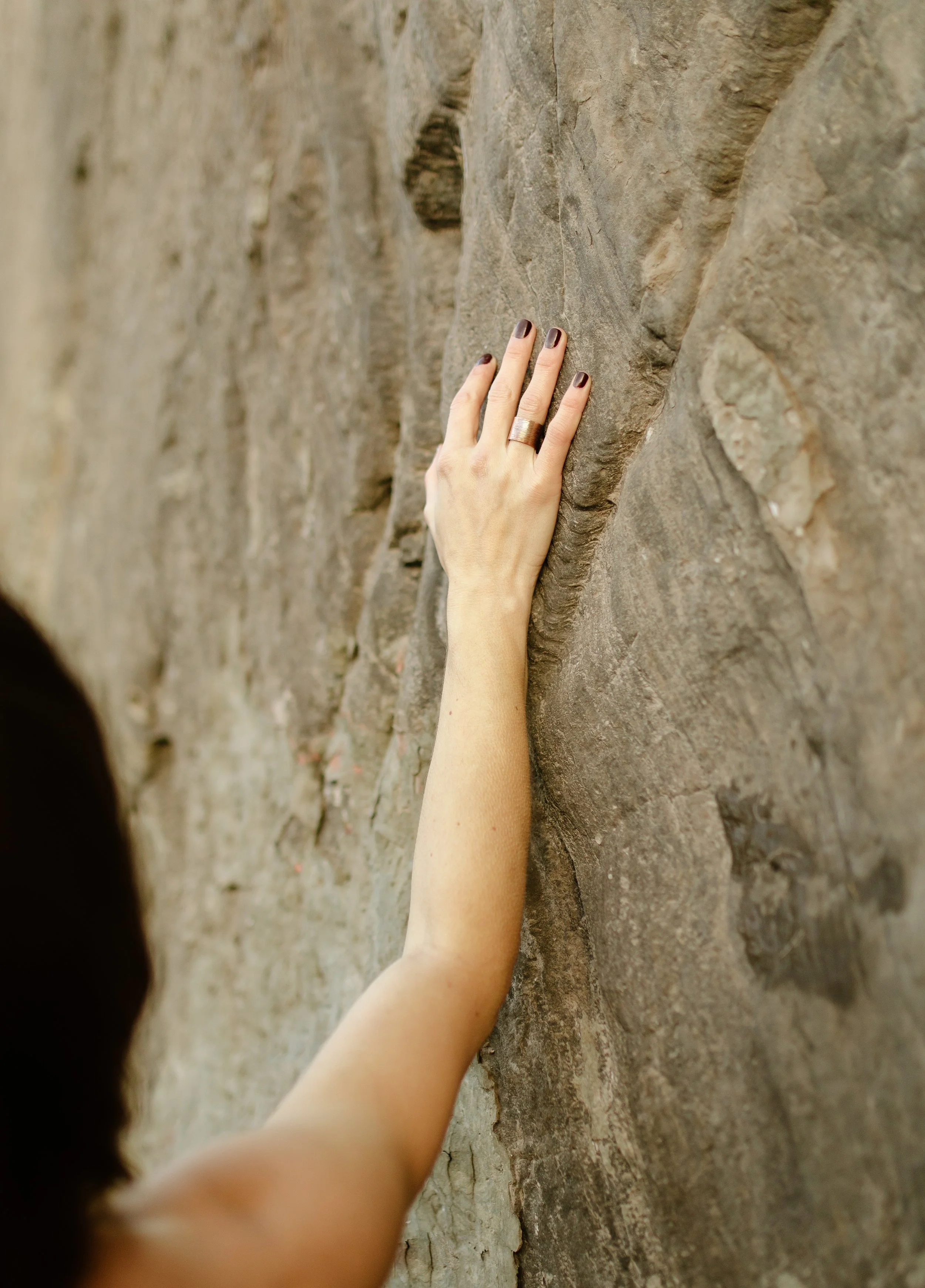 Close-up of a person's hand and arm reaching out and touching a textured stone wall.