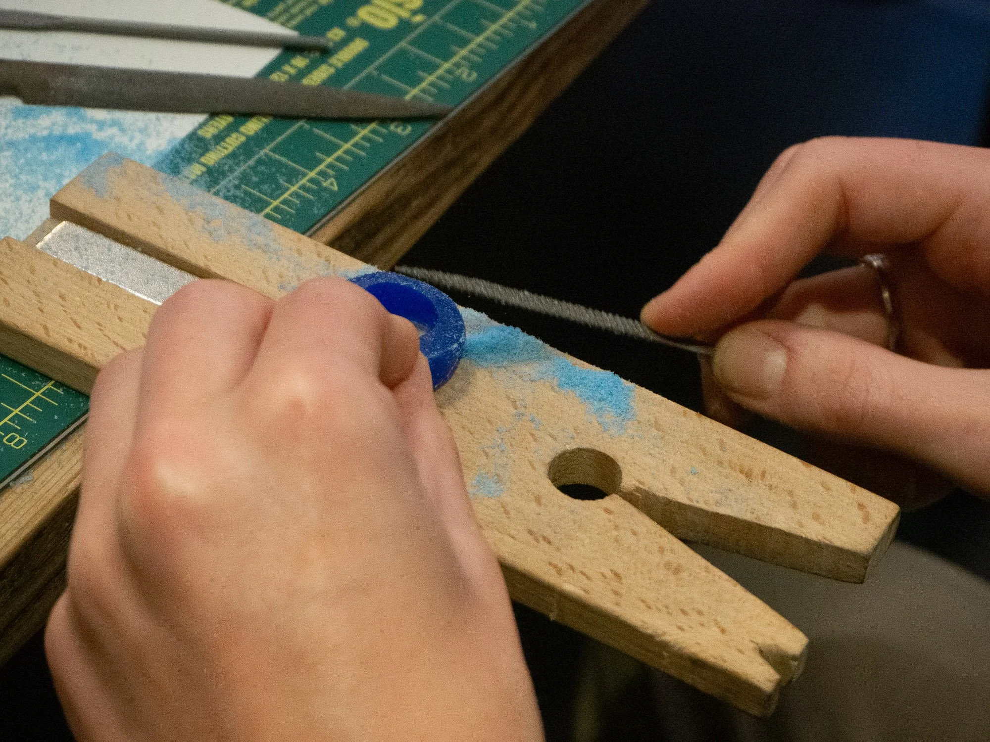 Person filing a small metal rod with a metal file, using a wooden bench pin.