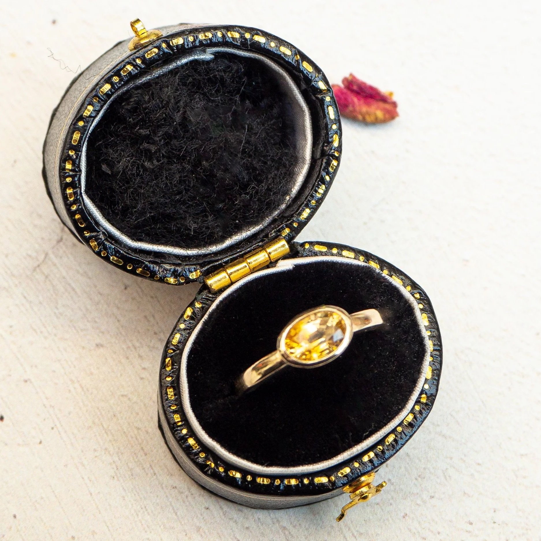 A close-up view of a black and gold jewelry box with a ring inside and a closed jewelry box open in the background.