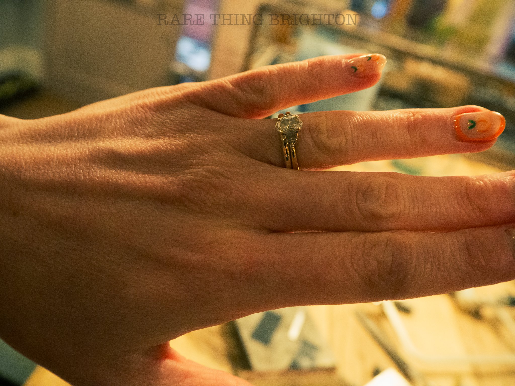 Close-up of a hand wearing a gold ring with a diamond, and nails painted with orange and black designs.