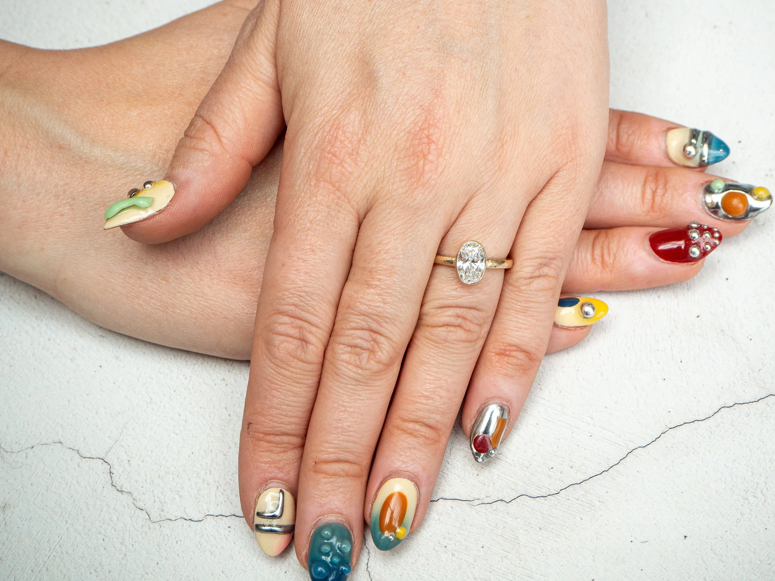 Close-up of a person's hand with colorful, decorated nail art and a gold ring with a large clear gemstone.
