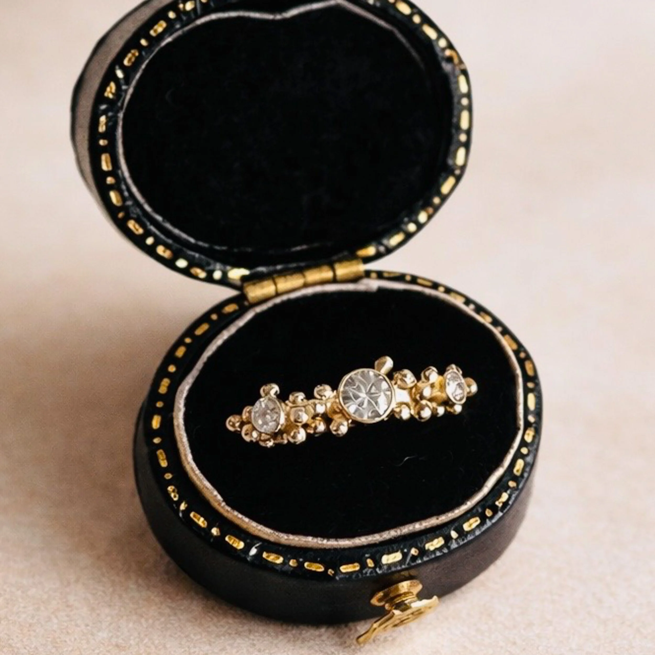 An open black jewelry box with gold accents and a string of gold-and-clear rhinestones inside, placed on a white surface.