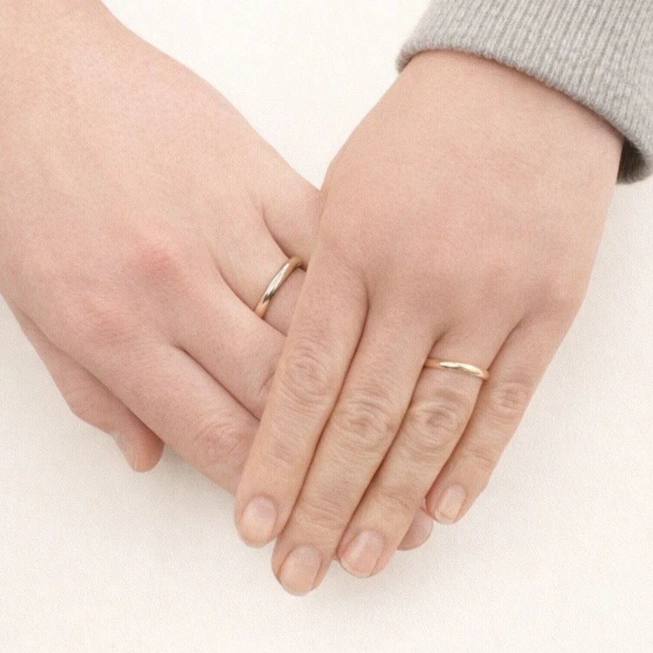 Two hands with wedding rings resting on a white surface, one hand has a gray sleeve.