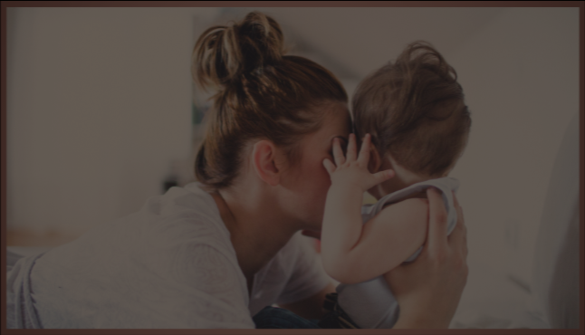 A woman holding and talking closely to a small child, face touching, in a cozy indoor setting.
