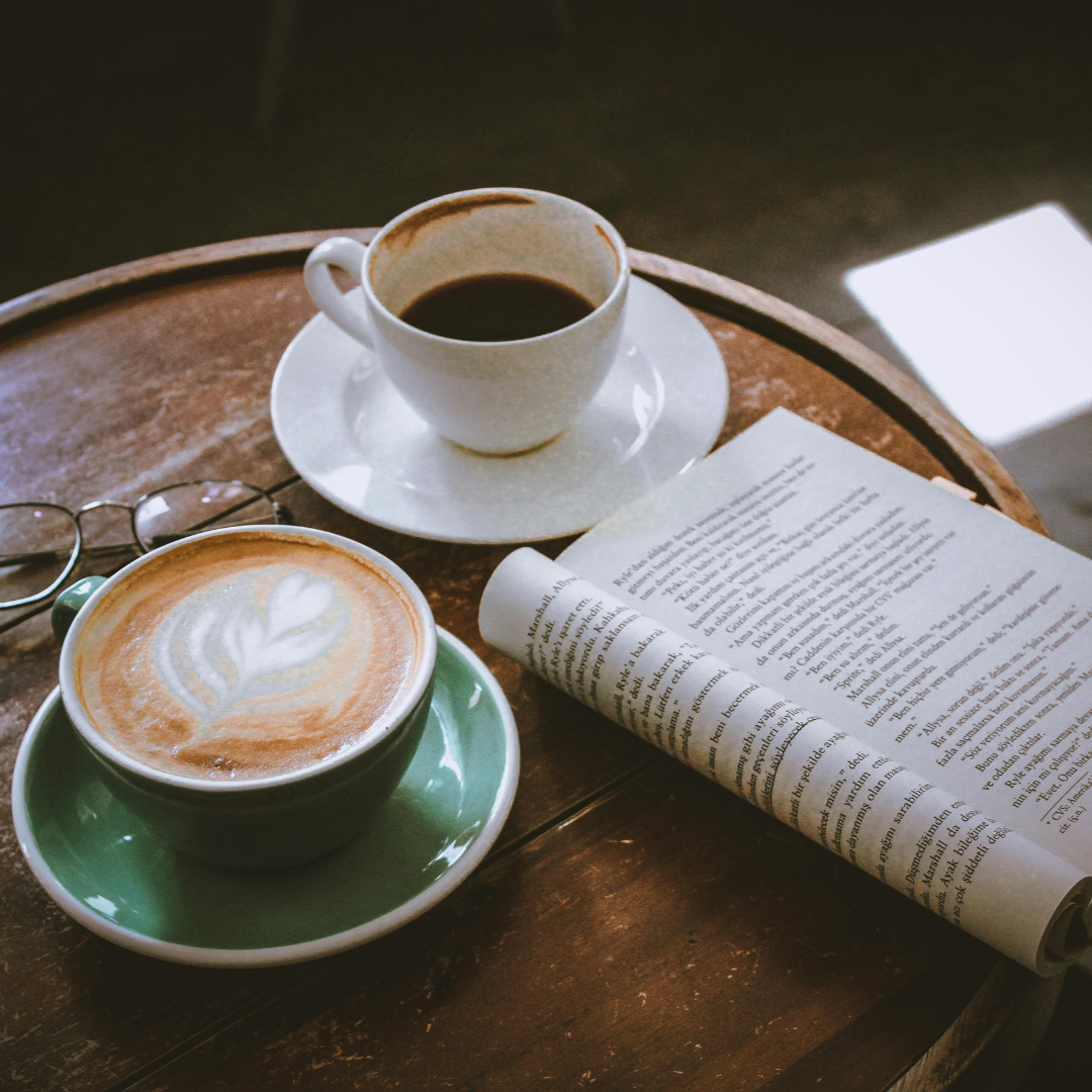 A wooden table with two cups of coffee, one with latte art and a newspaper, in a cozy setting.