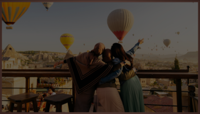 Three women on a balcony watching hot air balloons in the sky at sunrise or sunset.