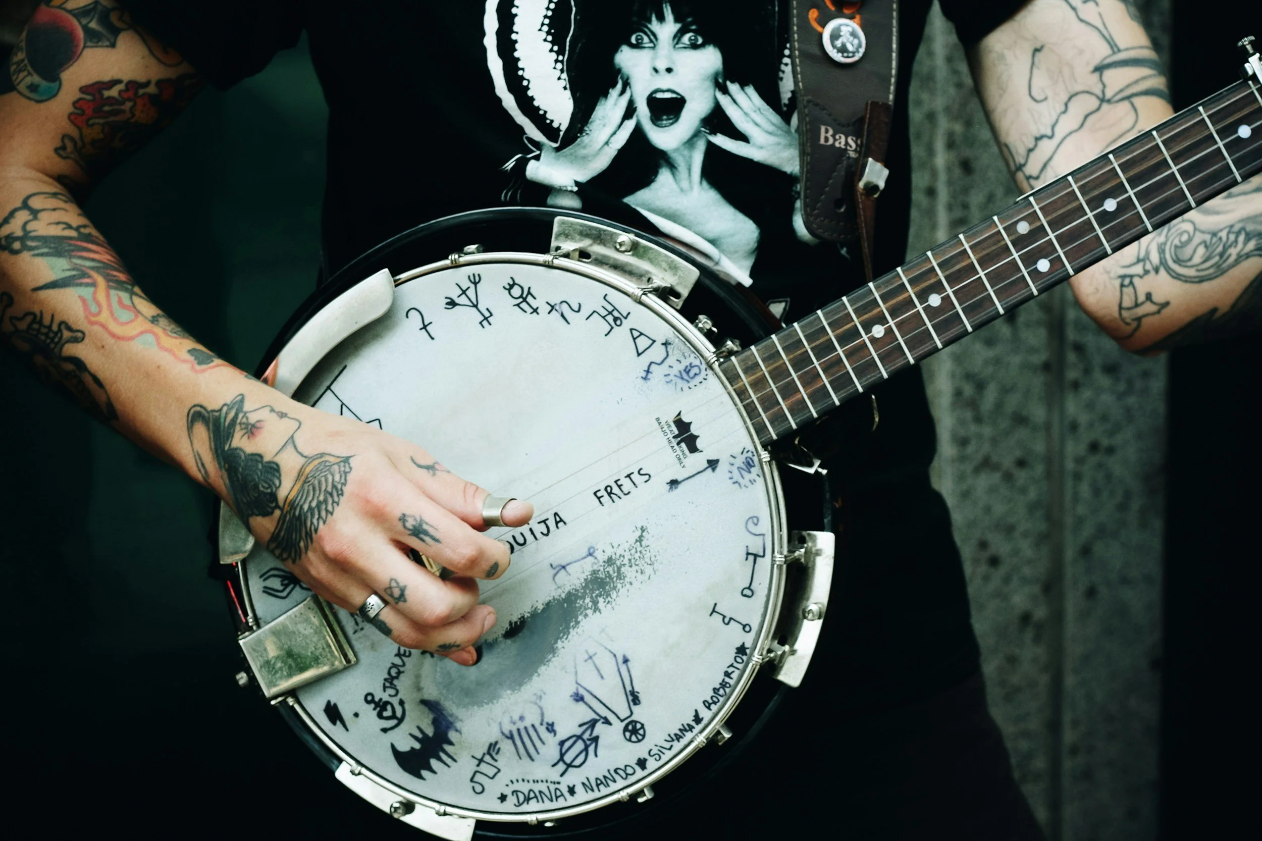 Tattooed person playing a banjo, wearing a black graphic T-shirt.