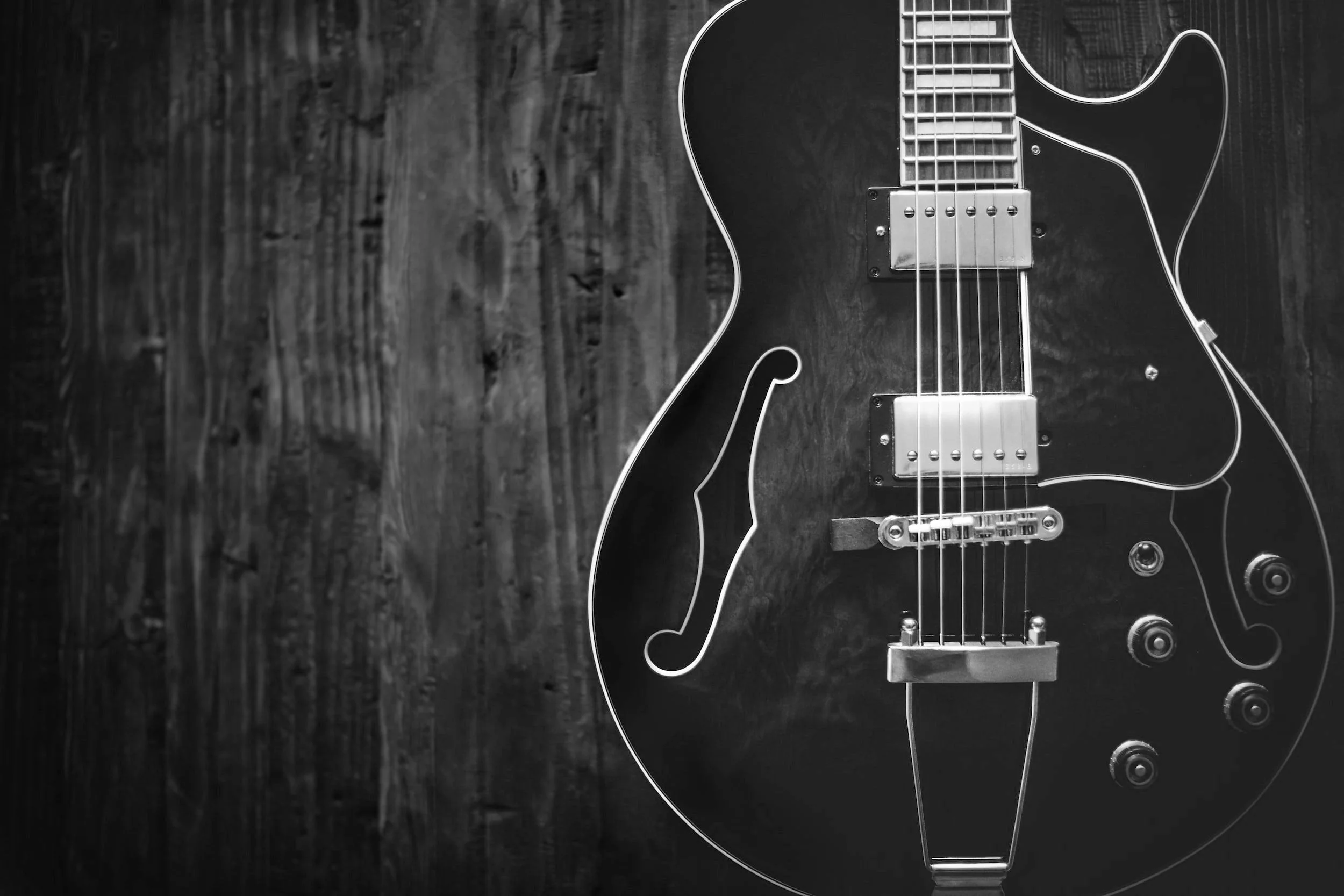 Black and white image of an electric guitar on a wooden background.