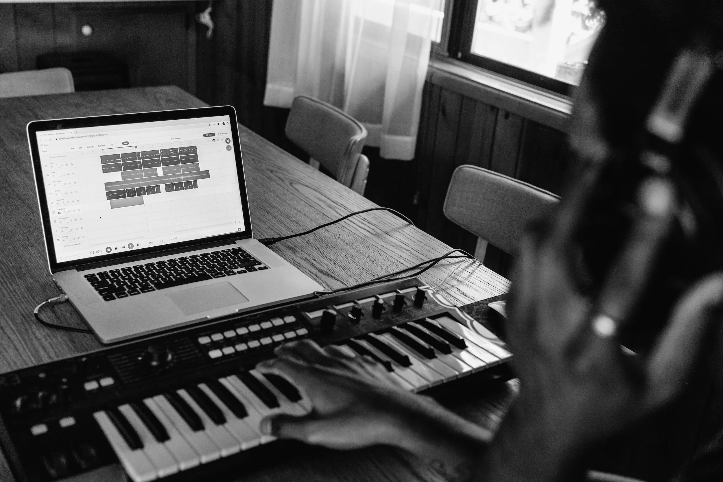 Person using a MIDI keyboard connected to a laptop with music production software.