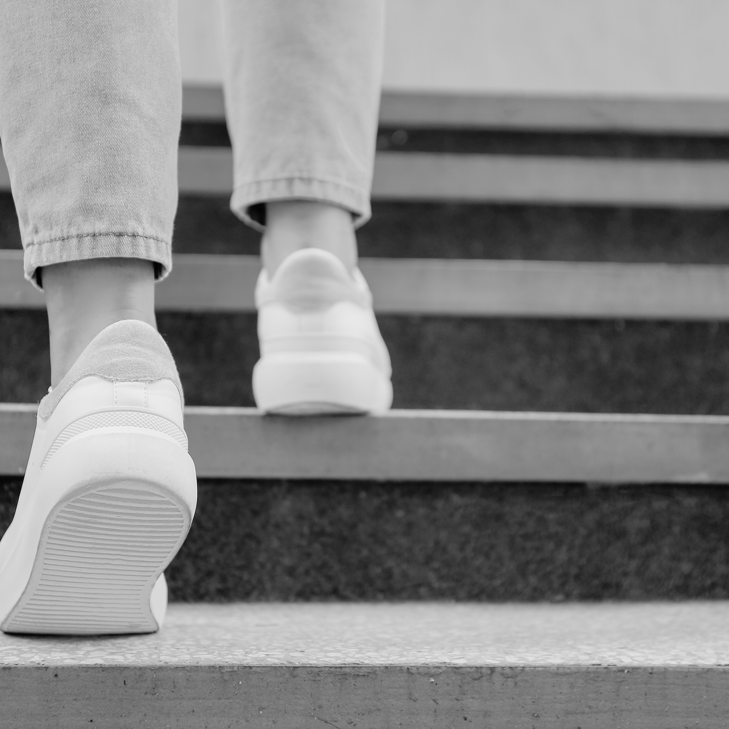 Black and white photo of someone's legs wearing jeans and sneakers, walking up a staircase.