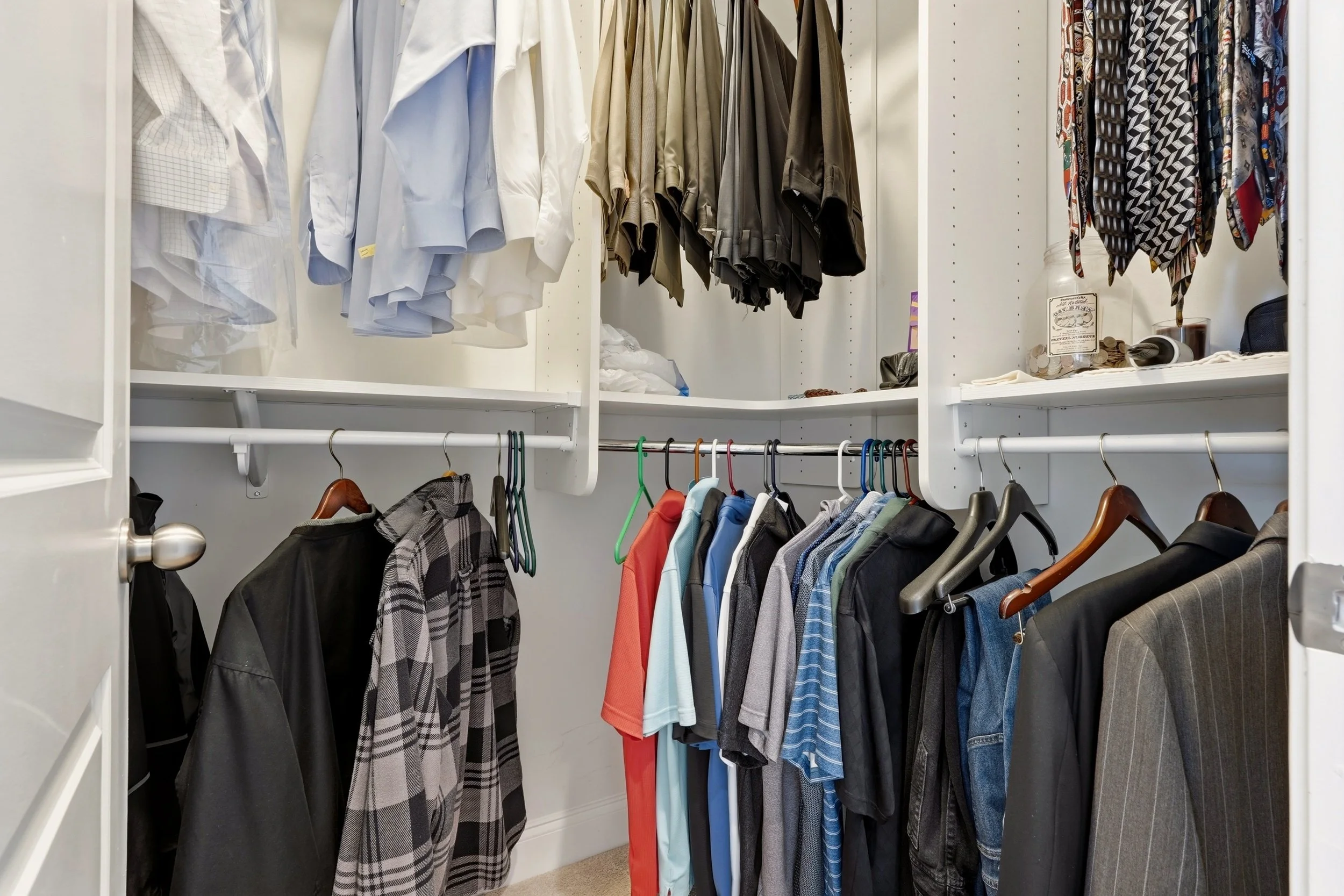 Closet with white, beige, black, and patterned clothing hanging on racks, organized by color and type.