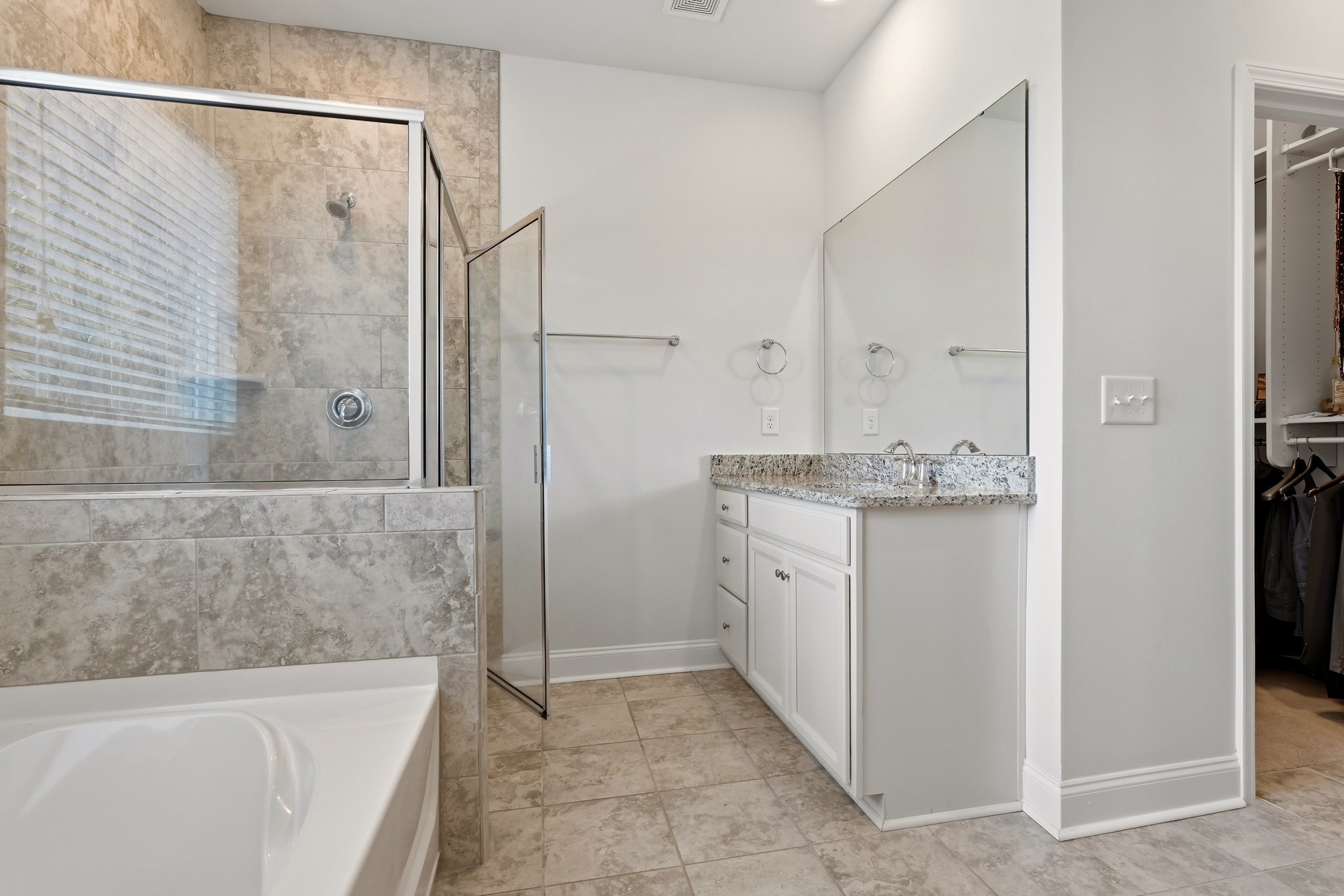 Bathroom with shower enclosure, vanity with granite countertop, large mirror, and closet with open door.