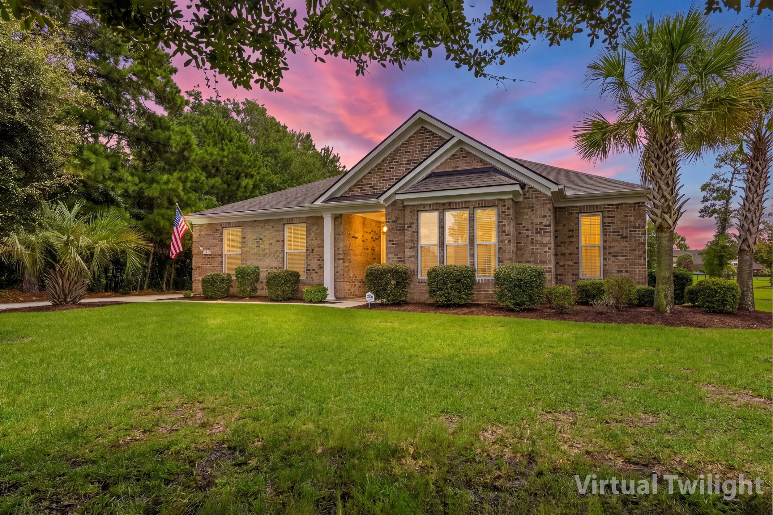 A brick house with a well-maintained lawn, surrounded by trees including palm trees, under a colorful sunset sky.