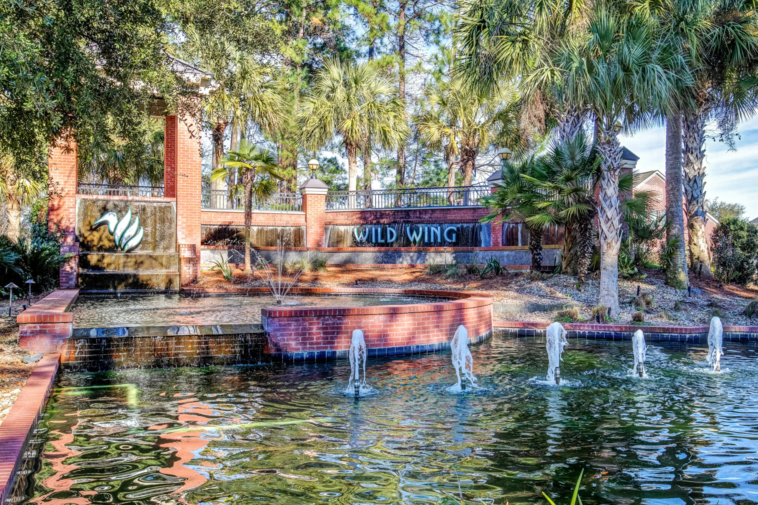 Water fountain at Wild Wing Plantation entrance with palm trees and greenery.