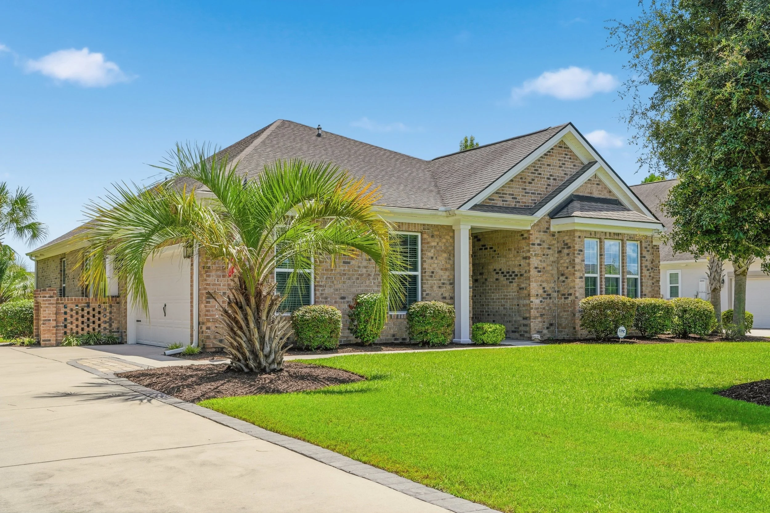 A brick house with a sloped roof, a white garage door, and well-maintained yard with green grass, shrubs, and trees.