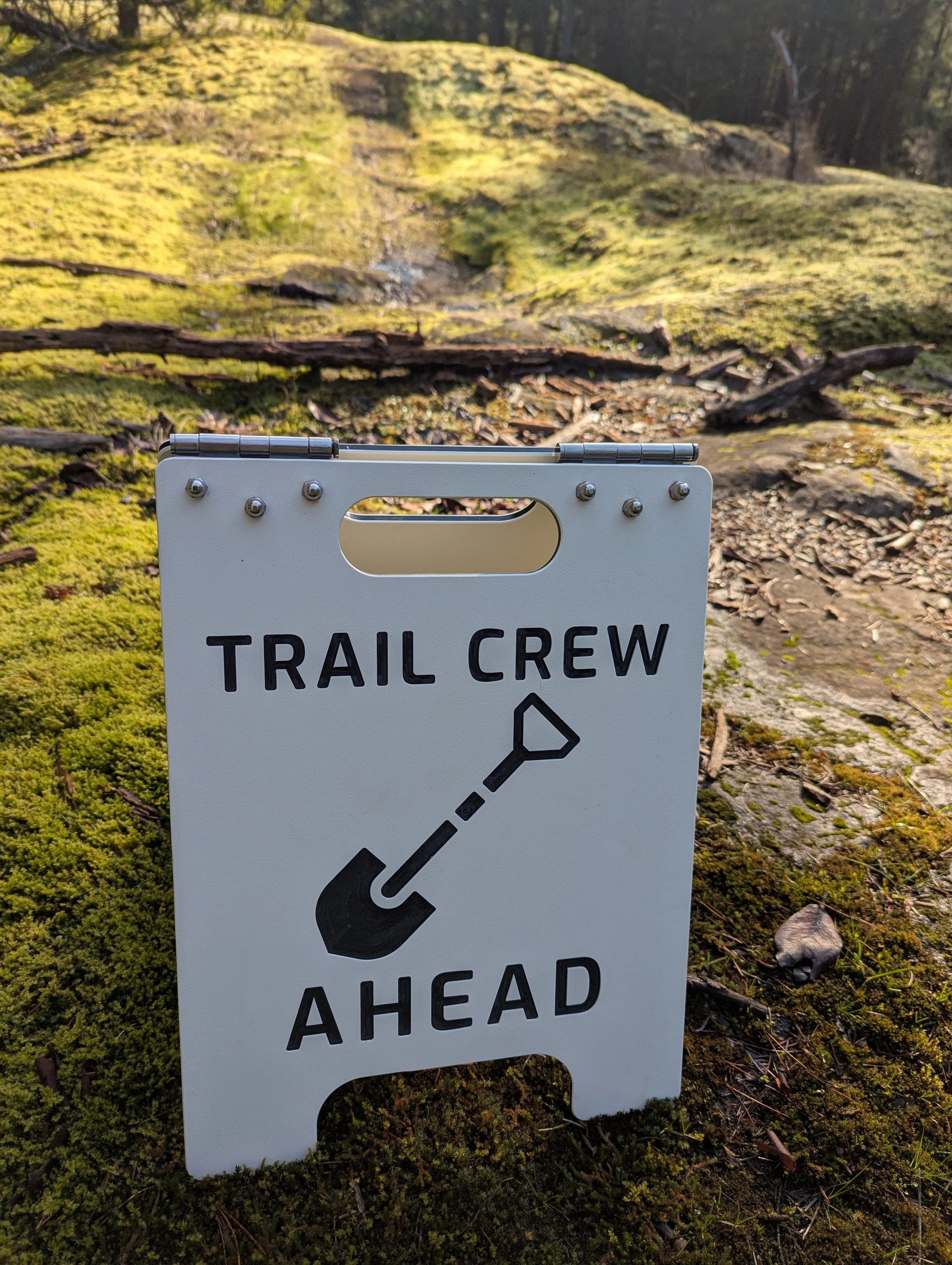 A sign stating Trail Crew Ahead with a shovel. Made from black and white King Colorcore. Shown in a natural setting.