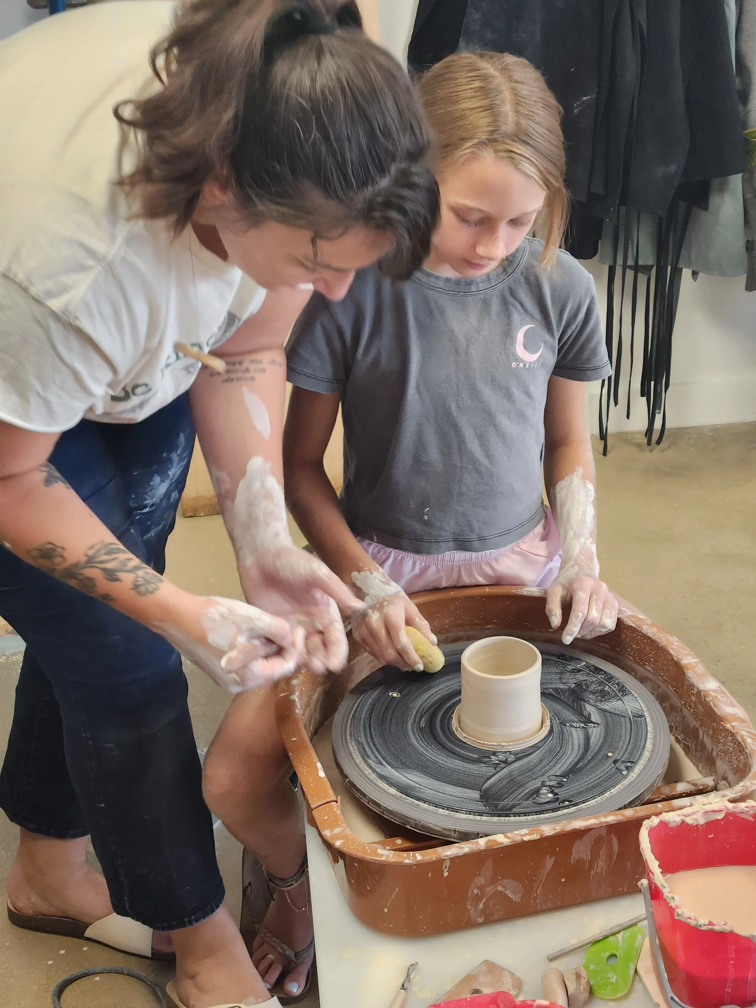 A ceramics instructor and a child working together on a pottery wheel to shape clay into a vessel at the art house st augustine