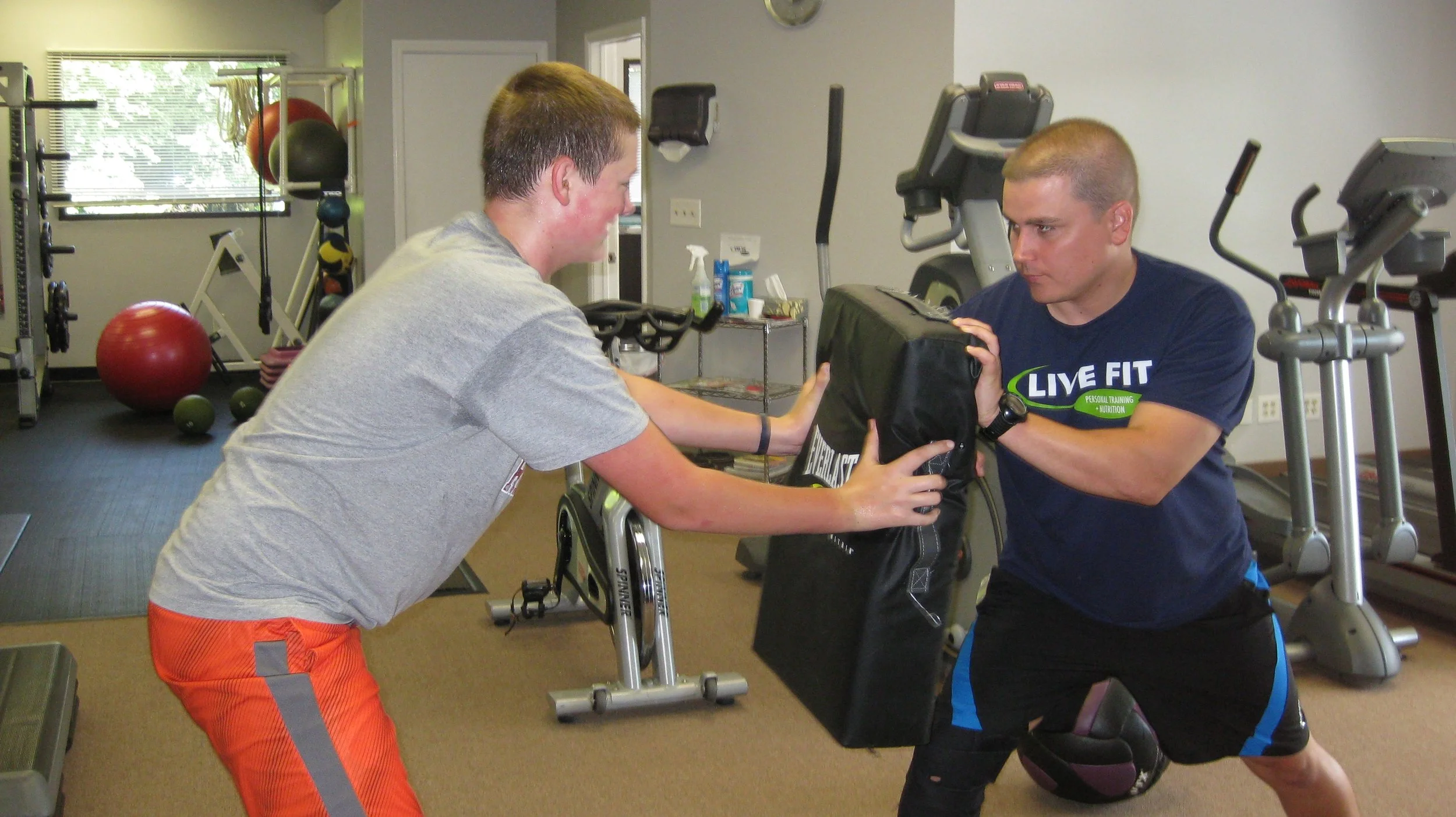 A personal trainer helping a young man develop strength and power in a fitness studio.