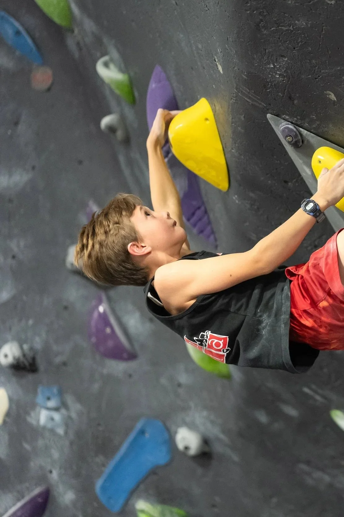 Young boy climbing on an indoor rock climbing wall with colorful holds.