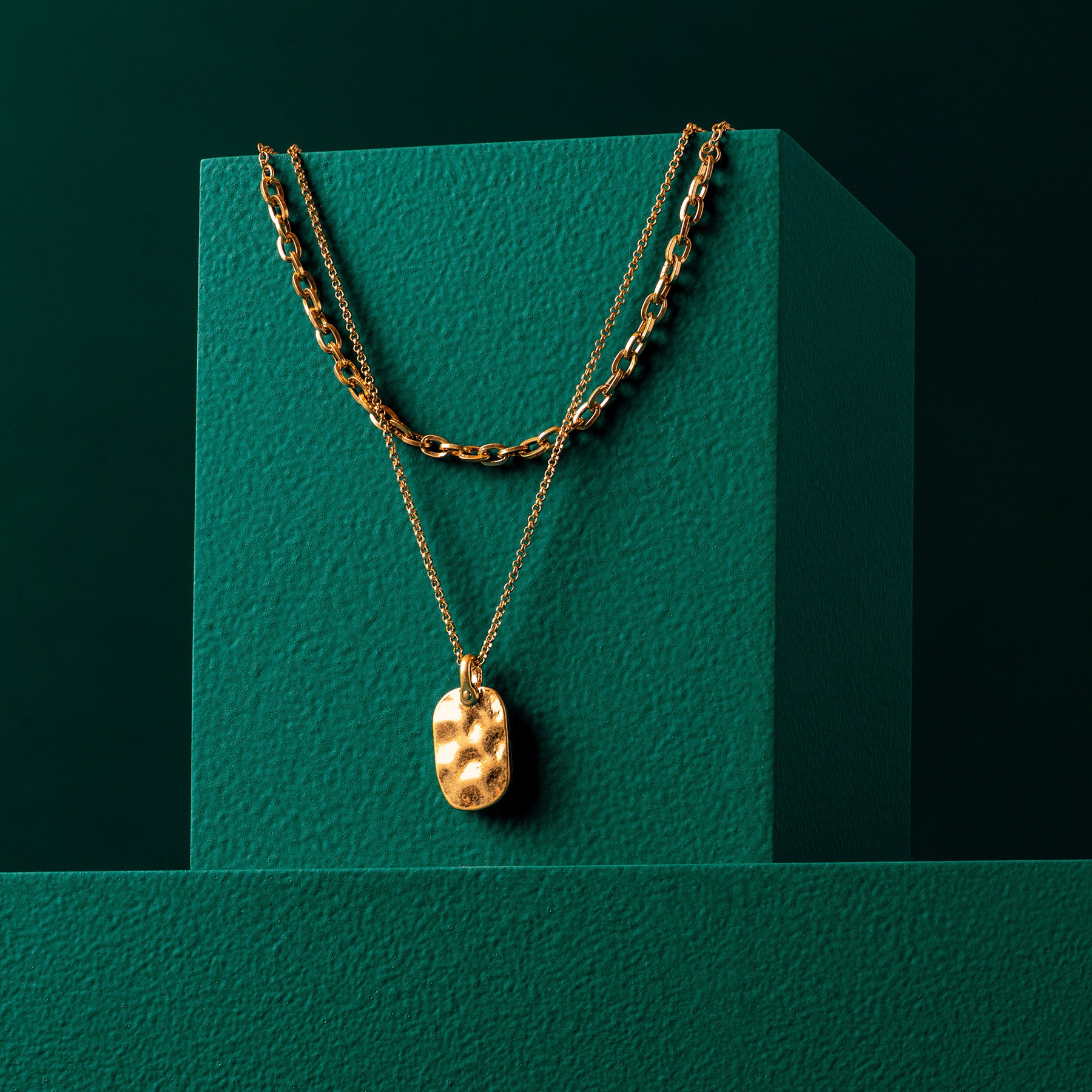 One green rectangular product photography riser displaying gold necklaces