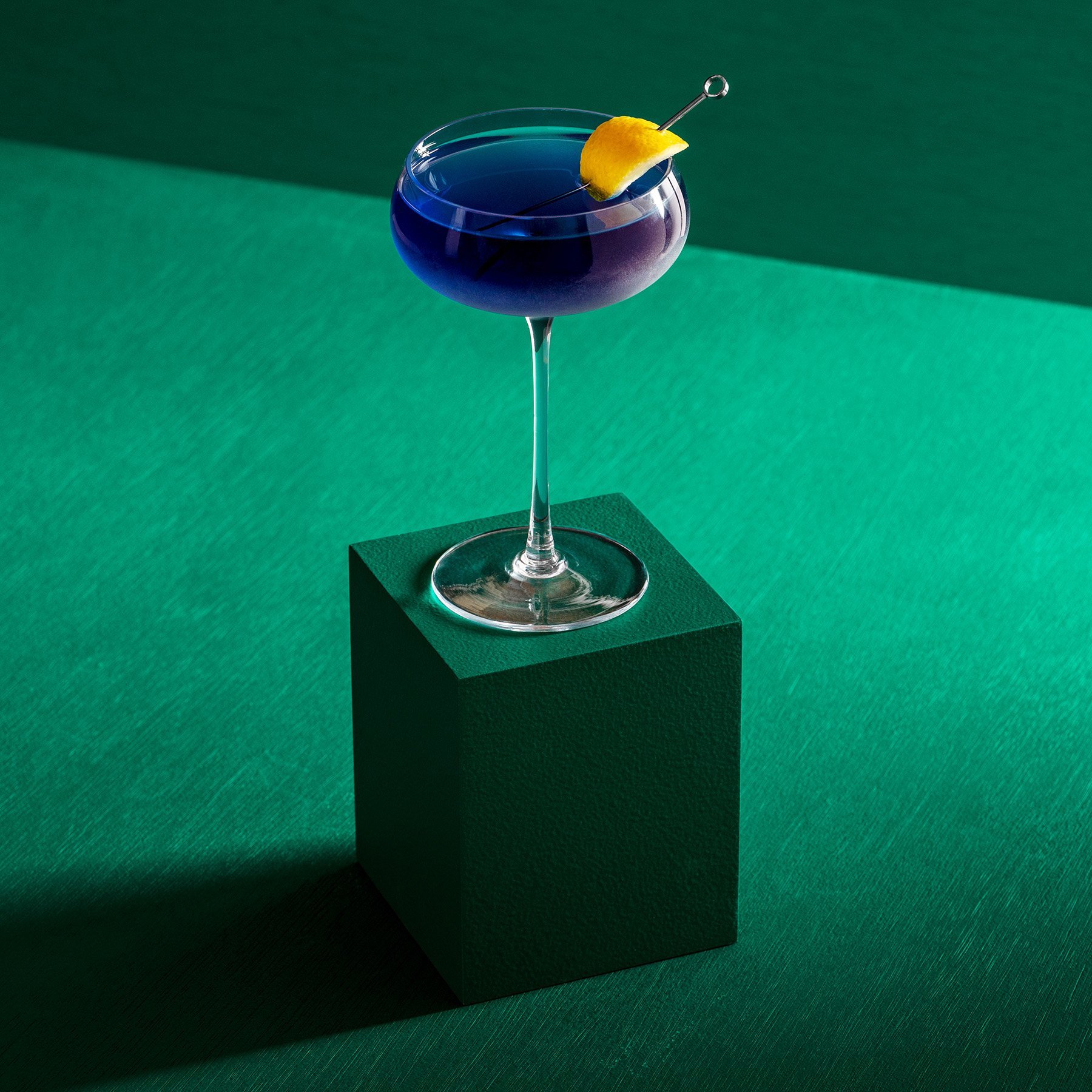 One green rectangular product photography riser displaying a purple cocktail in a fancy glass