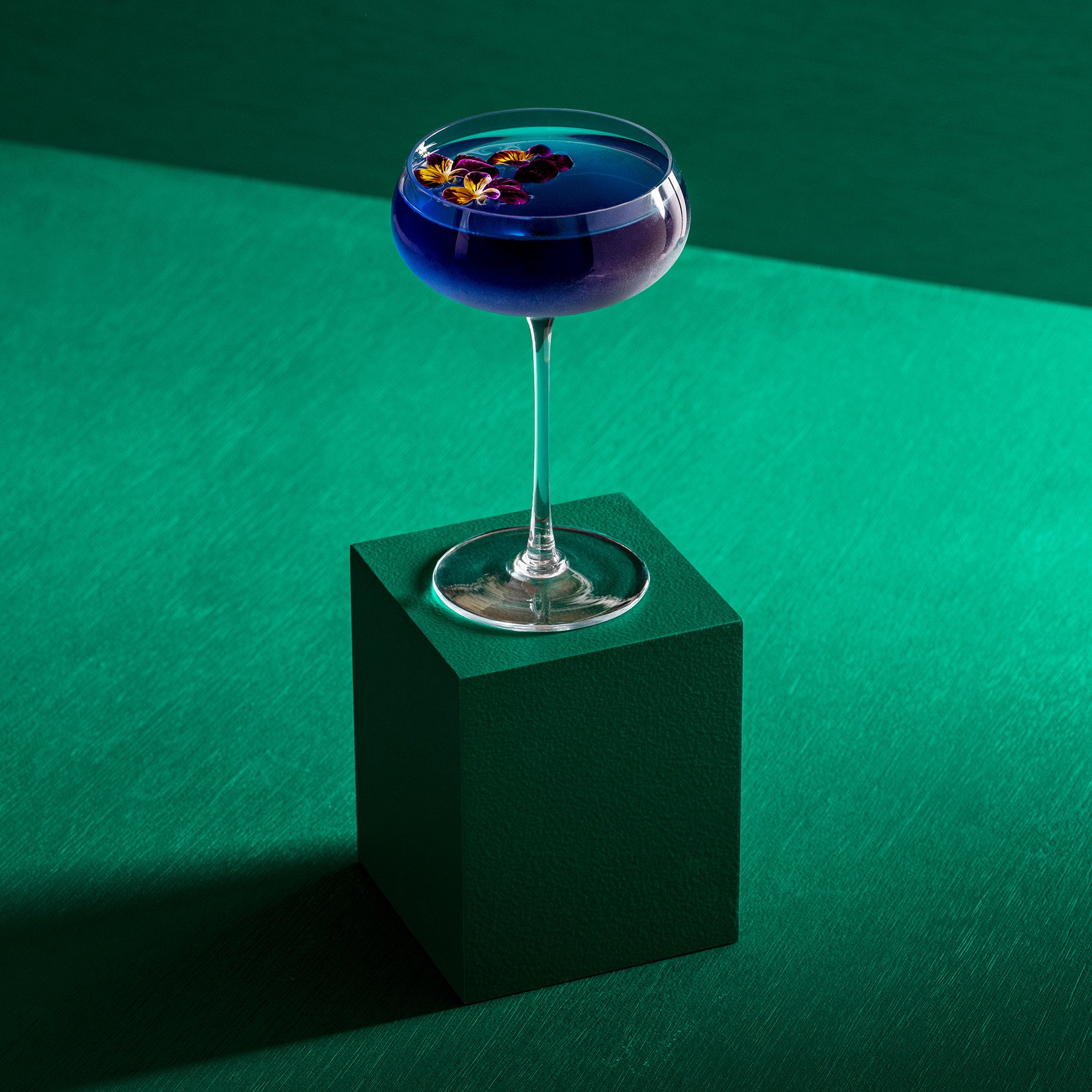 One green rectangular product photography riser displaying a purple cocktail in a fancy glass
