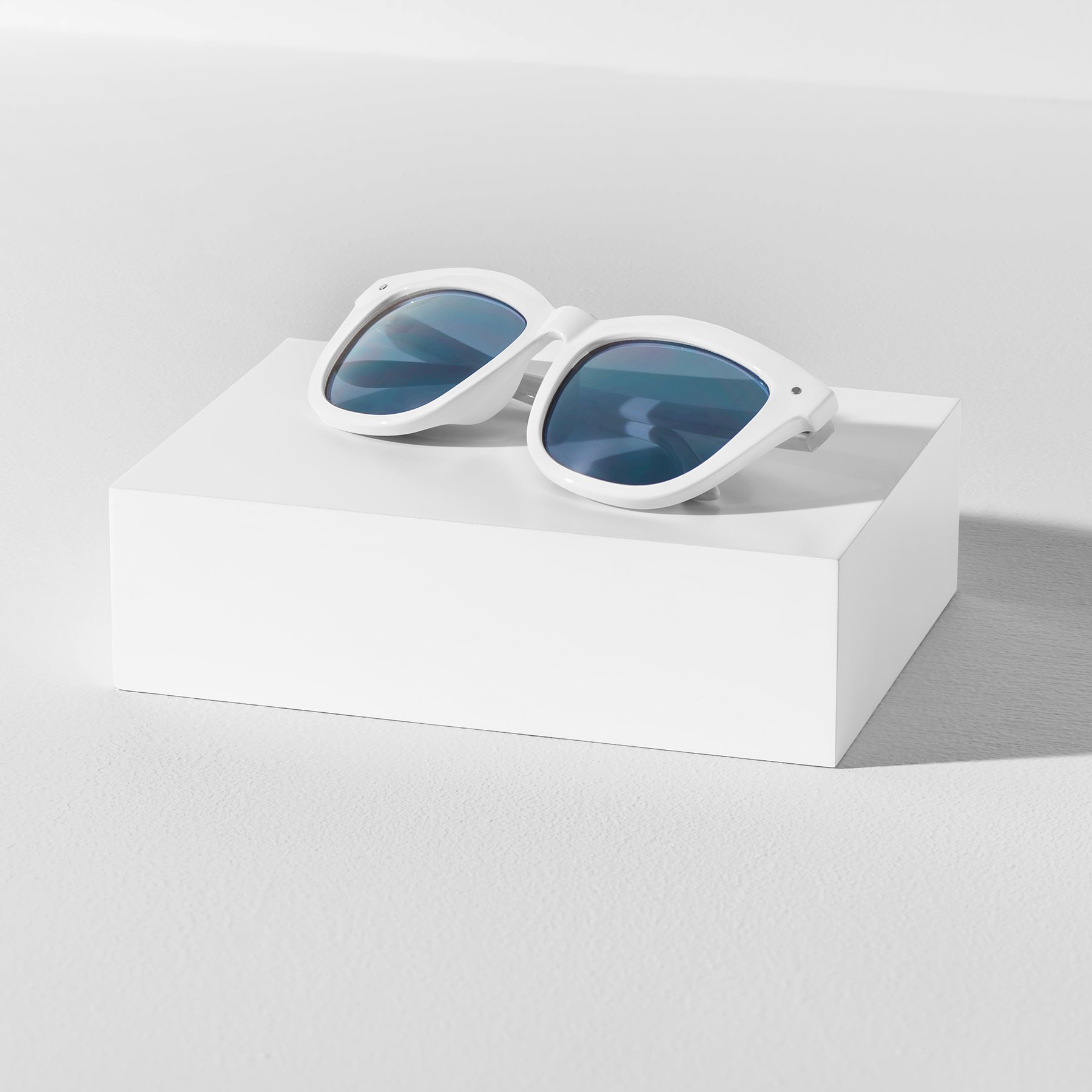 One rectangular white product photography riser displaying a pair of white sunglasses with blue lenses
